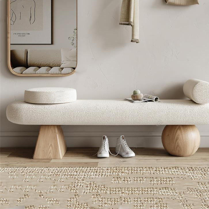 Cream boucle-upholstered 59-inch bench with round bolster and disc cushion, supported by solid light-wood cone and sphere legs, styled in a neutral coastal bedroom with mirror, hanging throw, sneakers and textured rug.