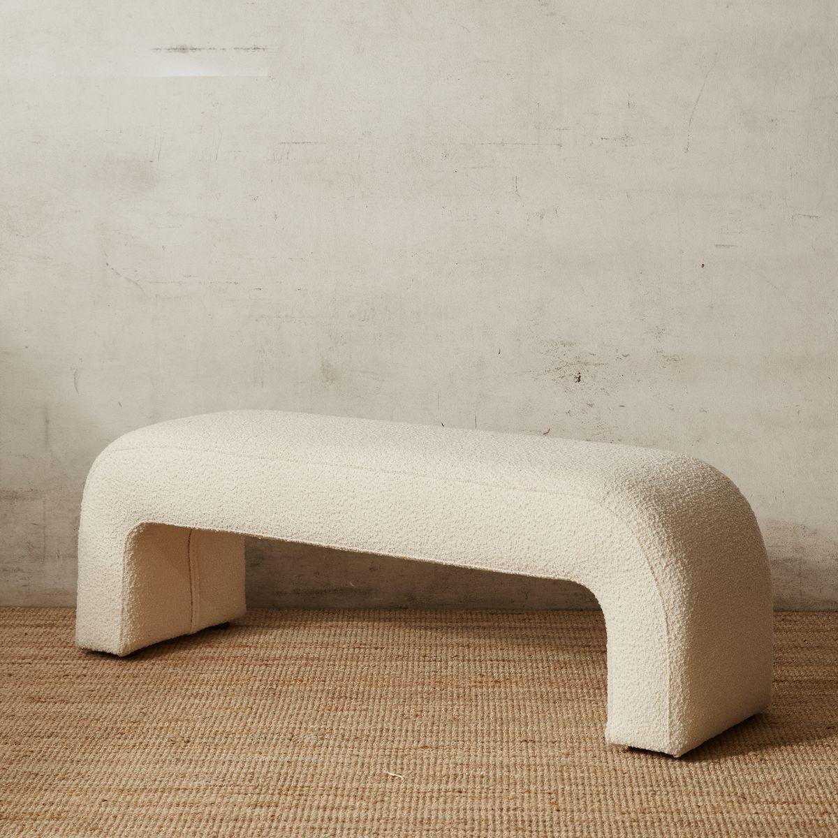 Cream boucle upholstered 75-inch end-of-bed bench with a rounded arch silhouette and integrated U-shaped legs, shown on a natural woven jute rug against a textured plaster wall.