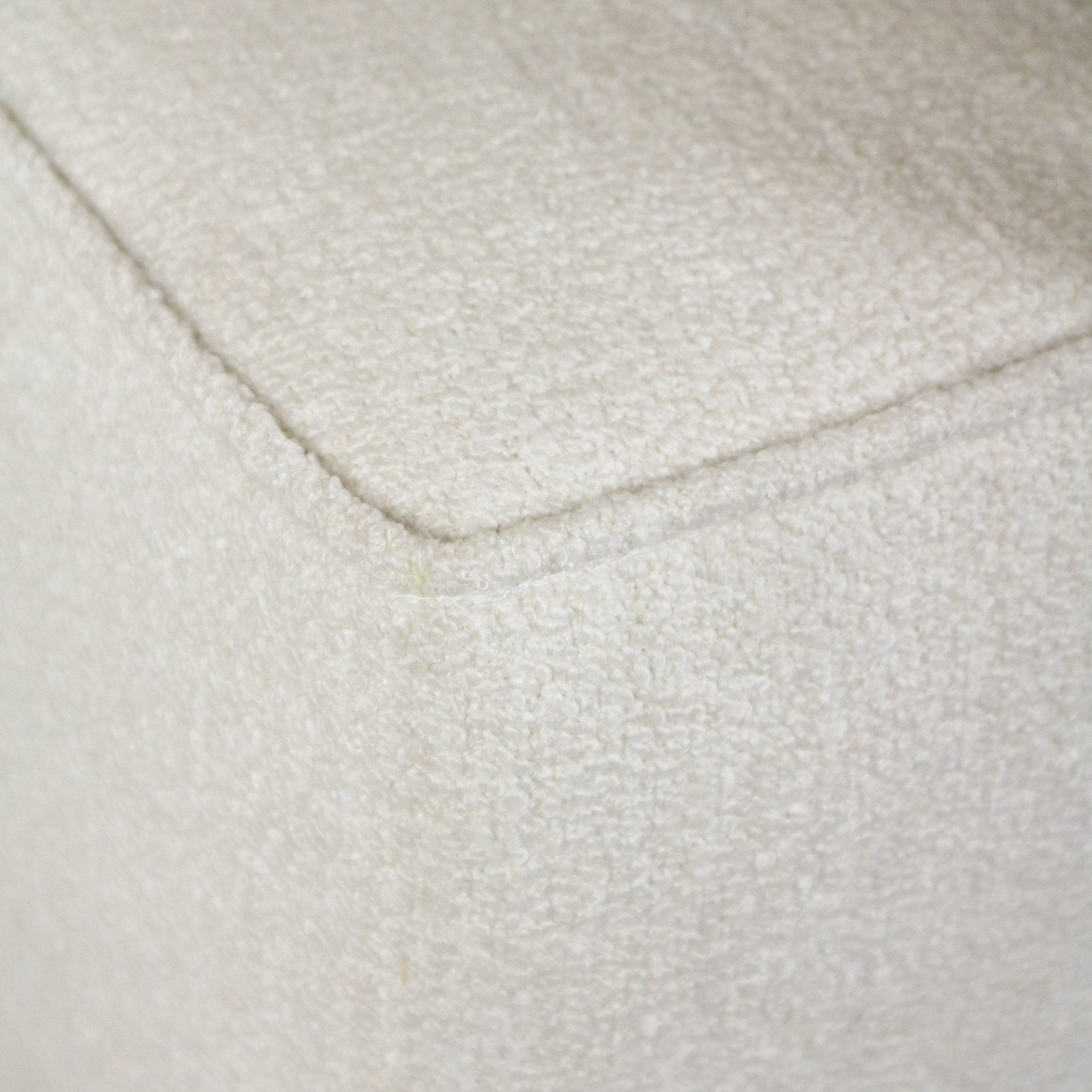 Close-up of cream boucle fabric on the corner of an upholstered end-of-bed bench, showing the looped texture and a neat piped seam detail.