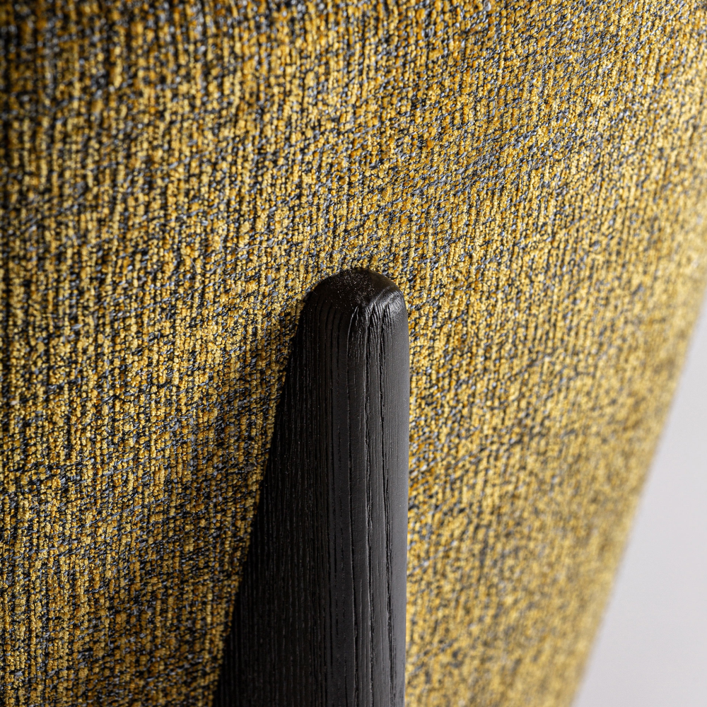 Close-up of mustard-yellow performance fabric upholstery on a dining chair back with a black-stained oak support, highlighting the textured woven fabric and visible wood grain.