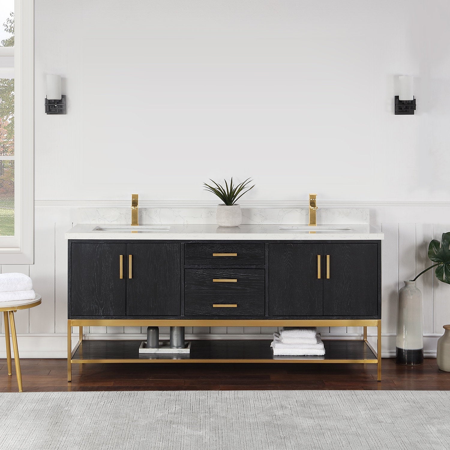 72-inch modern solid wood double-sink bathroom vanity with white stone countertop, black wood finish, gold metal base and matching gold faucets and handles, three center drawers, side cabinets and open lower shelf styled with towels and a plant.