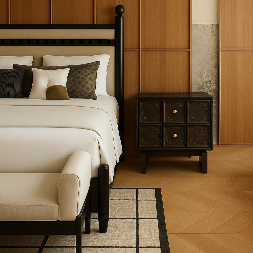 Dark solid walnut two-drawer nightstand with recessed circular drawer panels and brass knobs, styled beside a cream upholstered bed against warm wood-paneled walls.