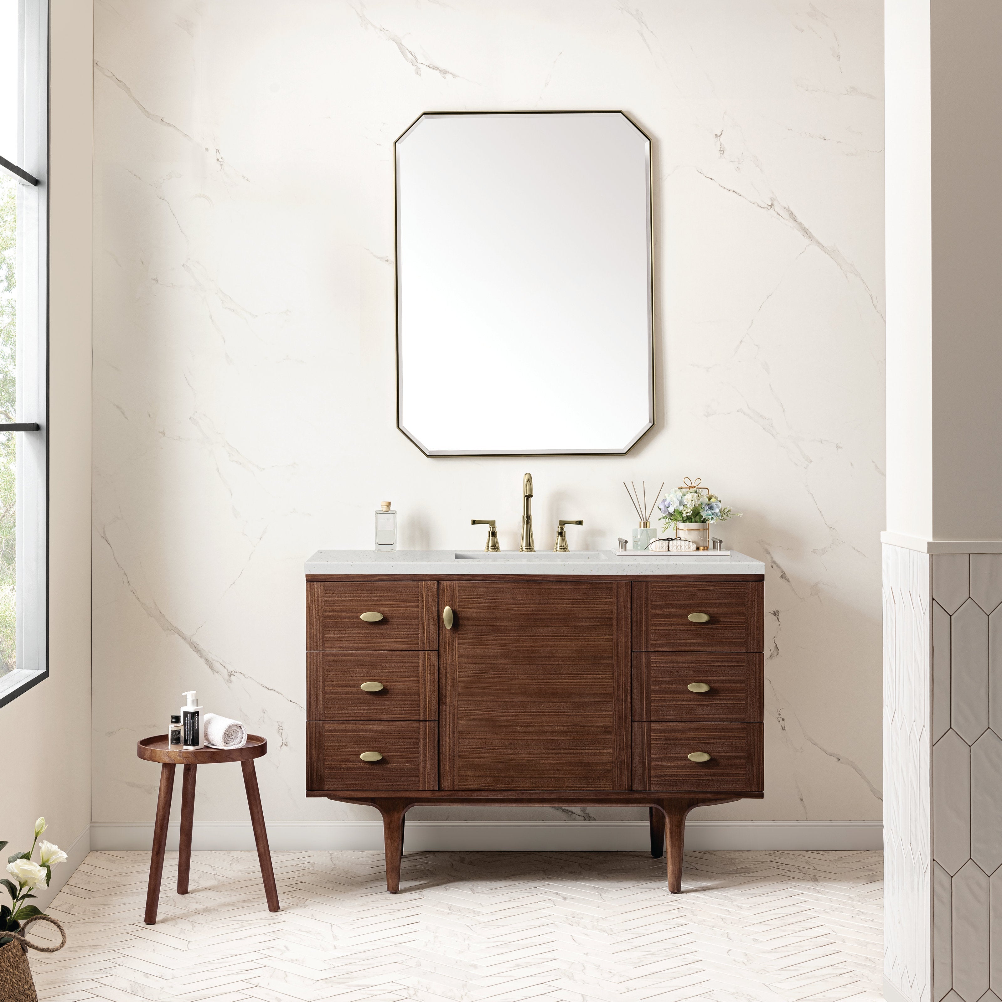 Freestanding mid-century walnut single-sink bathroom vanity with a stone quartz top, rectangular undermount sink, brass widespread faucet and oval brass pulls, six drawers and central cabinet on tapered legs beneath a framed mirror.