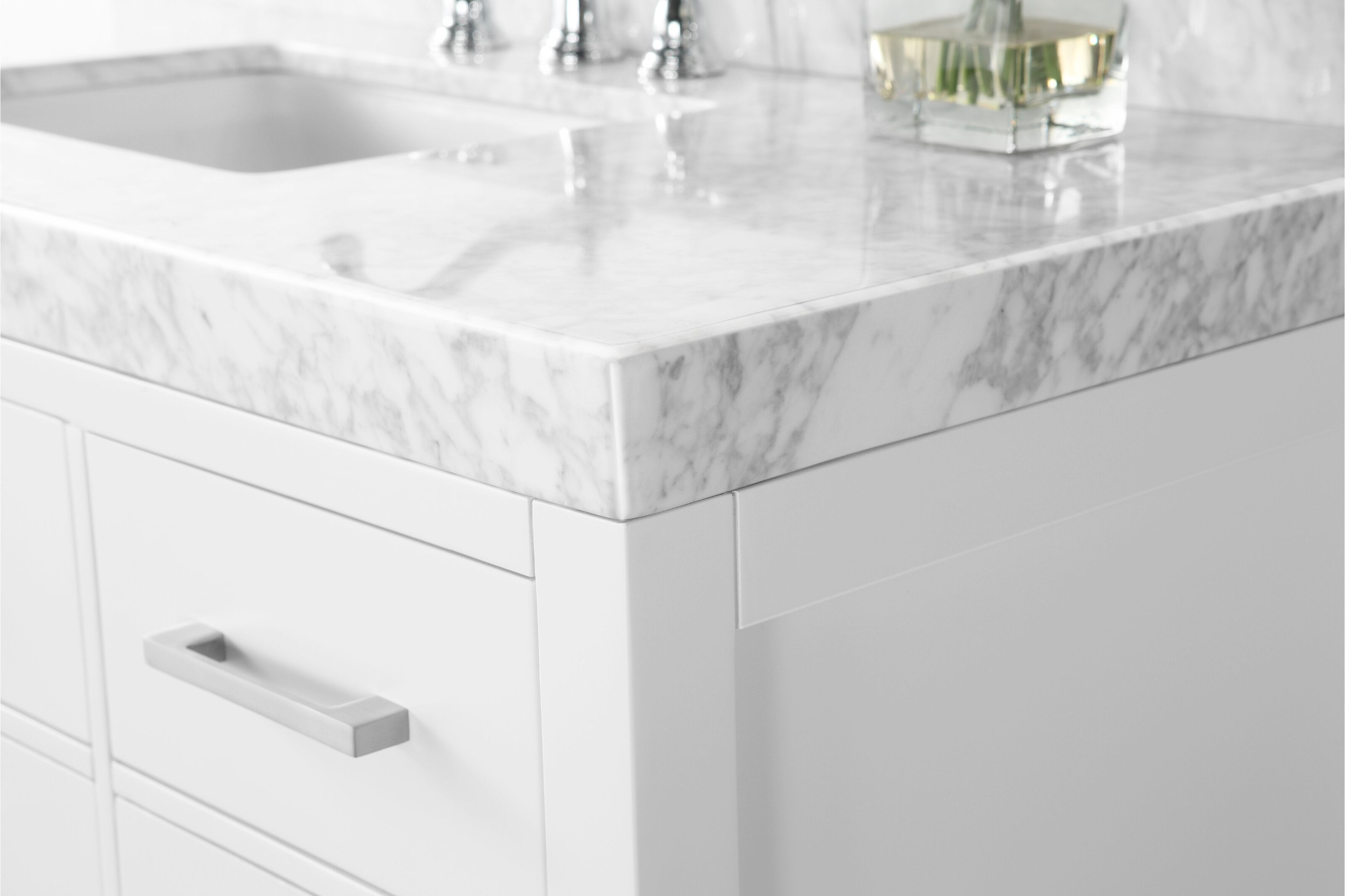Close-up of a stone marble countertop corner with integrated sink on a modern white solid-wood vanity, showing the marble edge, white cabinetry and a brushed metal drawer handle.