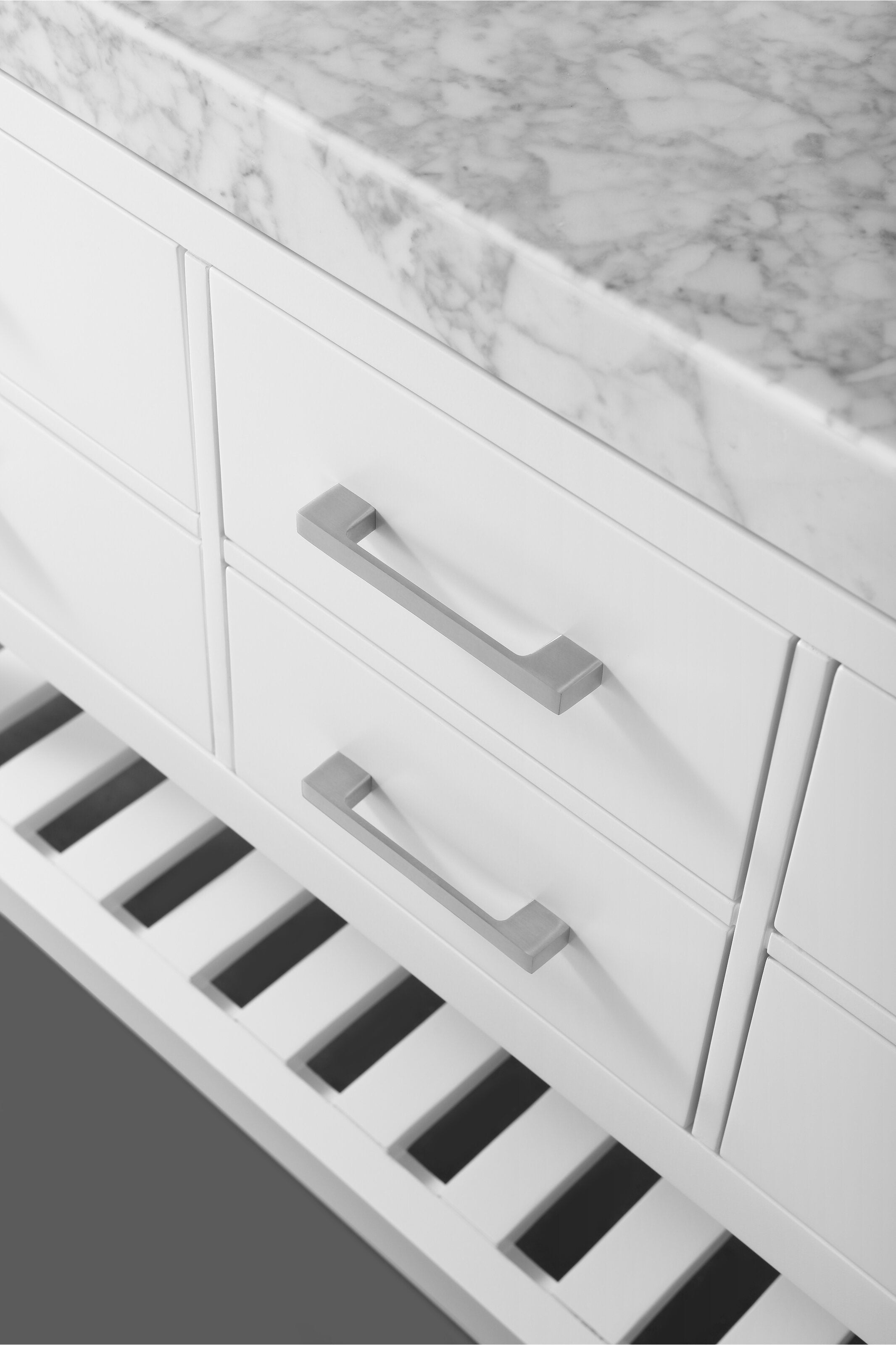 Close-up of a modern white solid wood bathroom vanity showing a marble stone top, two drawers with horizontal brushed metal handles and a slatted lower shelf.