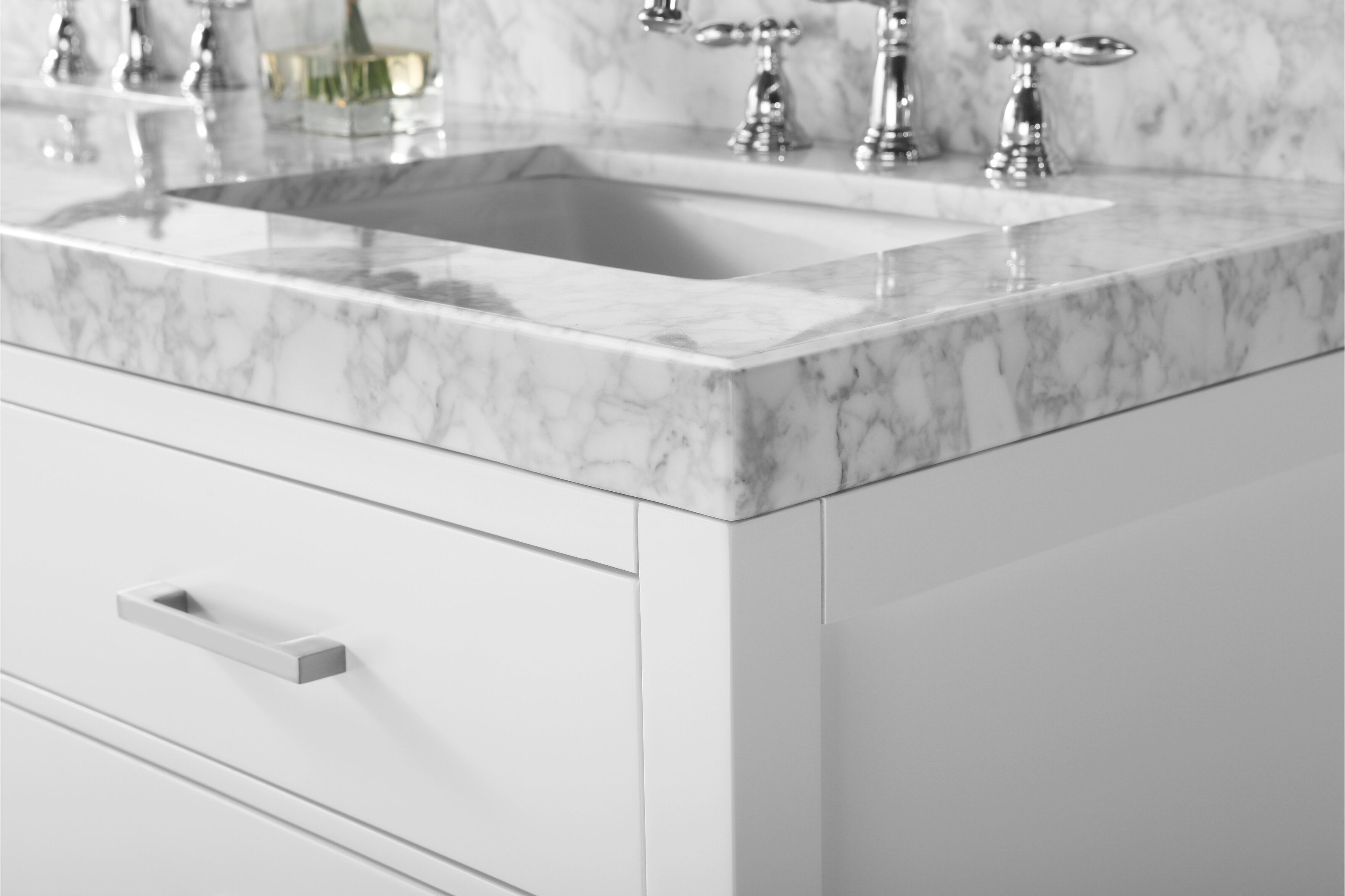 Close-up of a modern stone vanity corner showing a veined marble top with undermount ceramic sink, chrome faucets and a white solid wood cabinet drawer with a rectangular metal handle.