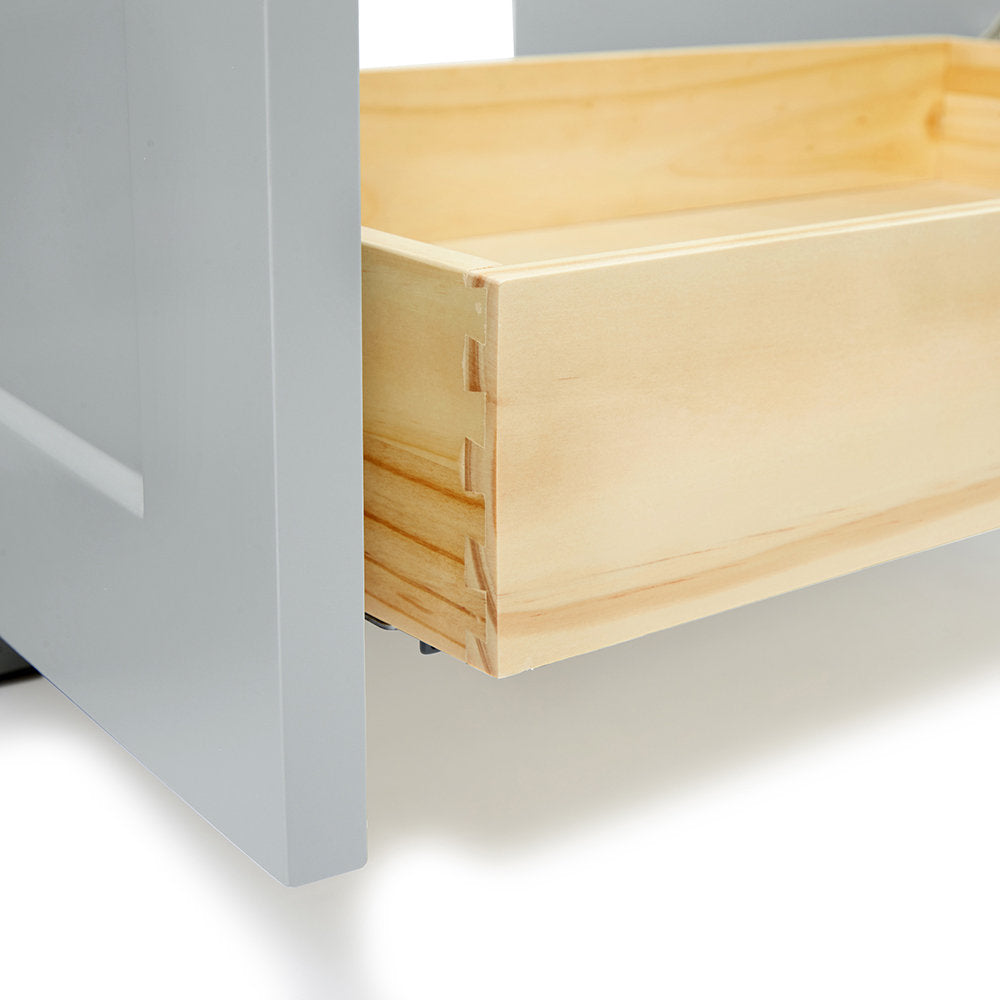Close-up of a natural solid wood vanity drawer showing dovetail joinery and light wood interior, paired with a gray-painted cabinet side and a visible metal drawer slide.