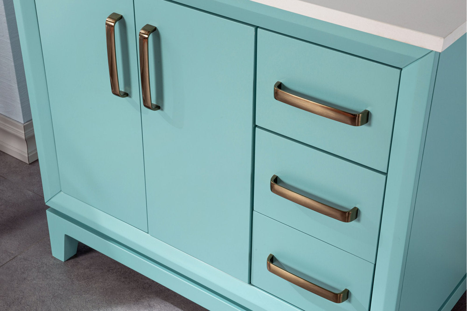 Close-up of an aqua-painted solid wood bathroom vanity with a white stone countertop, three right-side drawers and double doors on the left, all fitted with brushed brass handles.