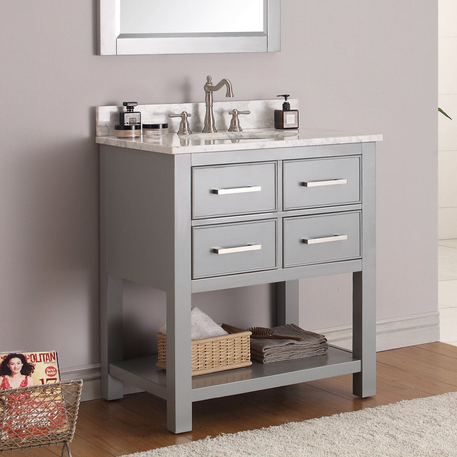 Freestanding modern gray solid-wood bathroom vanity with stone marble top and backsplash, single undermount sink, brushed-nickel faucet, four drawer fronts with horizontal metal pulls and lower shelf with basket and towels.