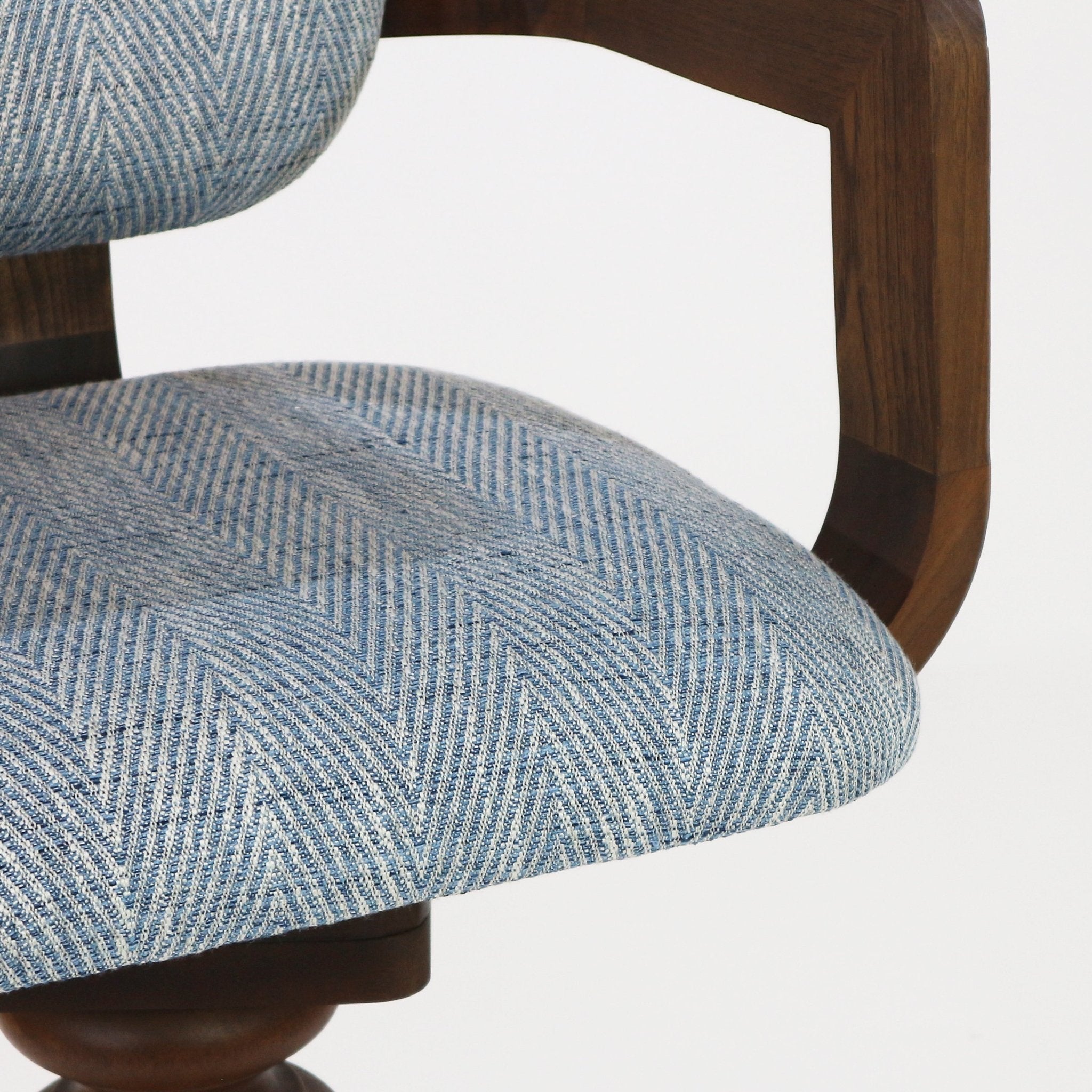 Close-up of a light blue herringbone fabric upholstered bar-stool seat showing the textured cushion and a curved natural wood arm and partial turned wooden swivel base.