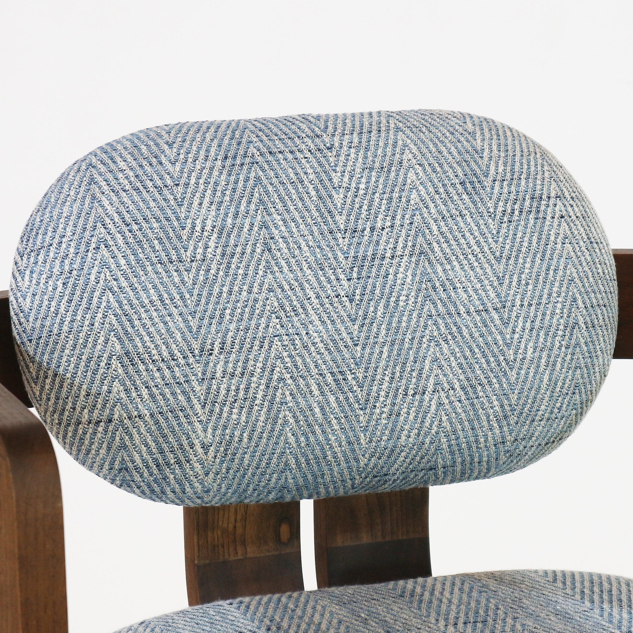 Close-up of a rounded bar stool backrest upholstered in blue and light-gray herringbone fabric, supported by dark natural wood slats with a portion of the matching upholstered seat visible at the bottom.