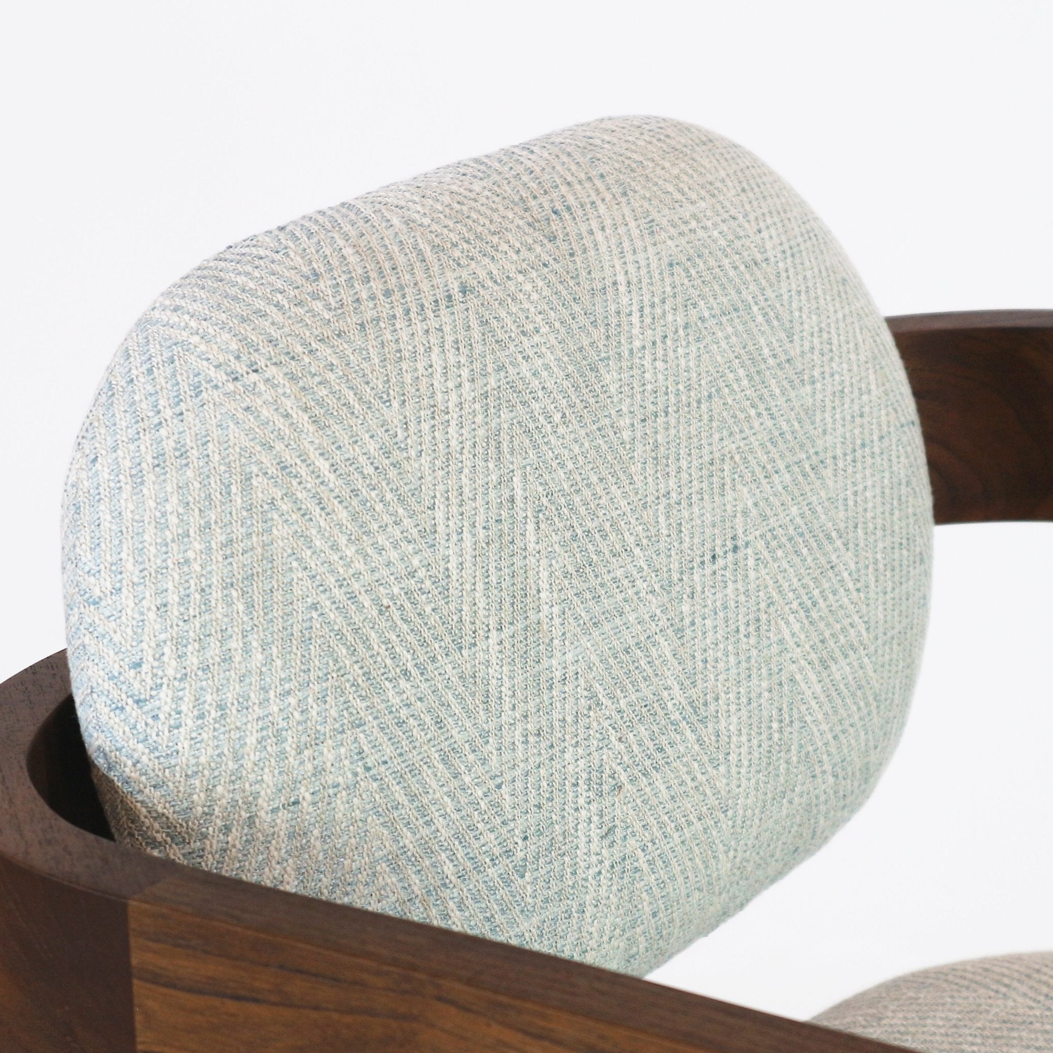 Close-up of a light blue-gray textured fabric backrest with subtle herringbone weave set into a curved dark wood frame of a modern bar stool.