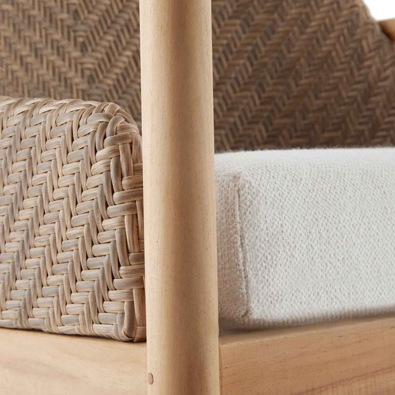 Close-up of a natural teak round arm and woven wicker back beside a cream fabric seat cushion on a coastal outdoor dining chair, highlighting wood grain and textured weave.