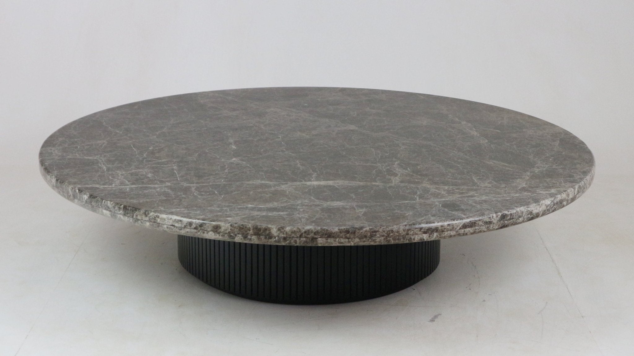 Low round coffee table with a dark veined marble top and a black fluted wooden base, shown on a neutral studio floor.
