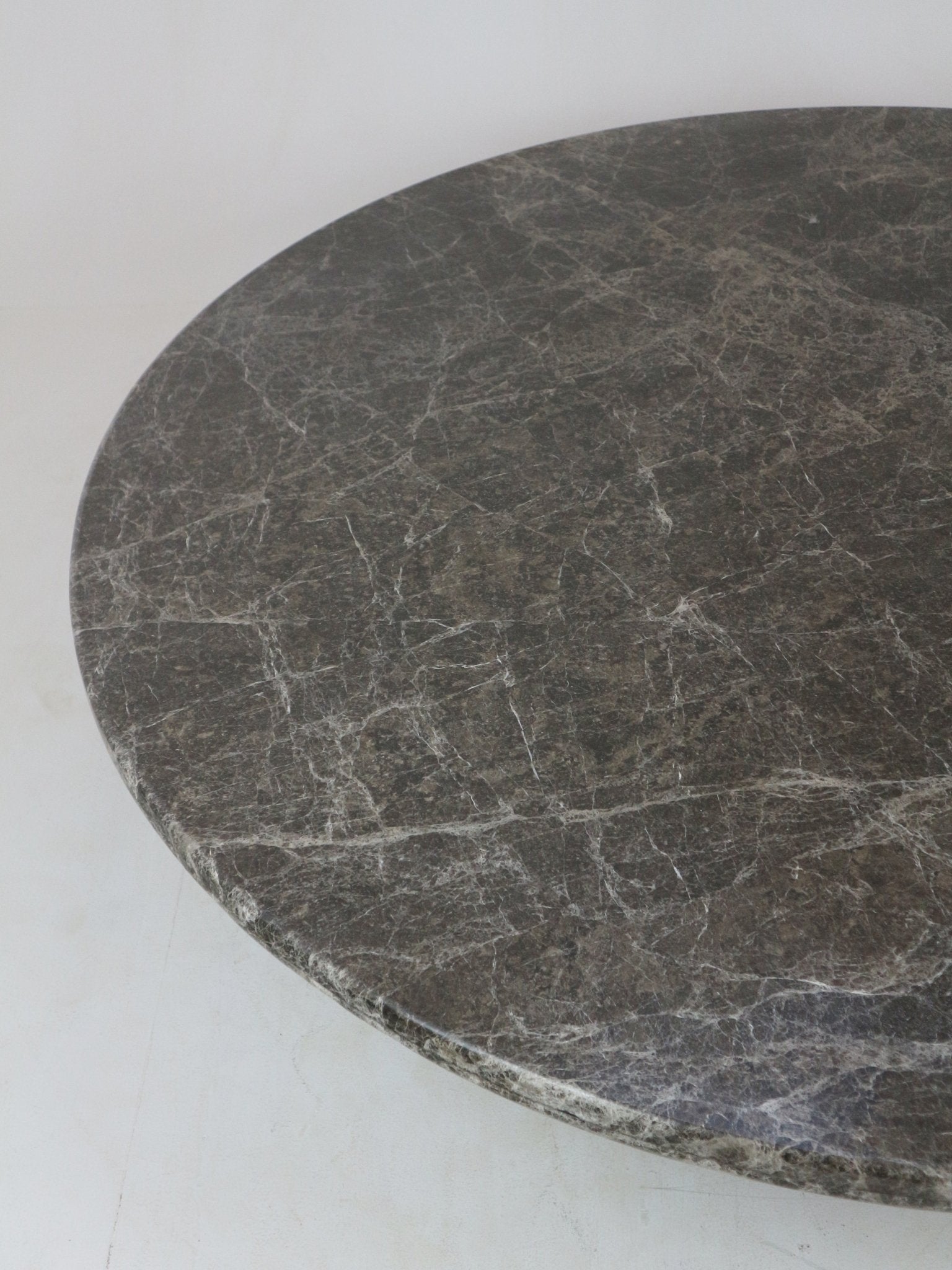 Close-up view of a round black marble coffee table top with white veining and a polished edge, photographed on a light neutral surface.