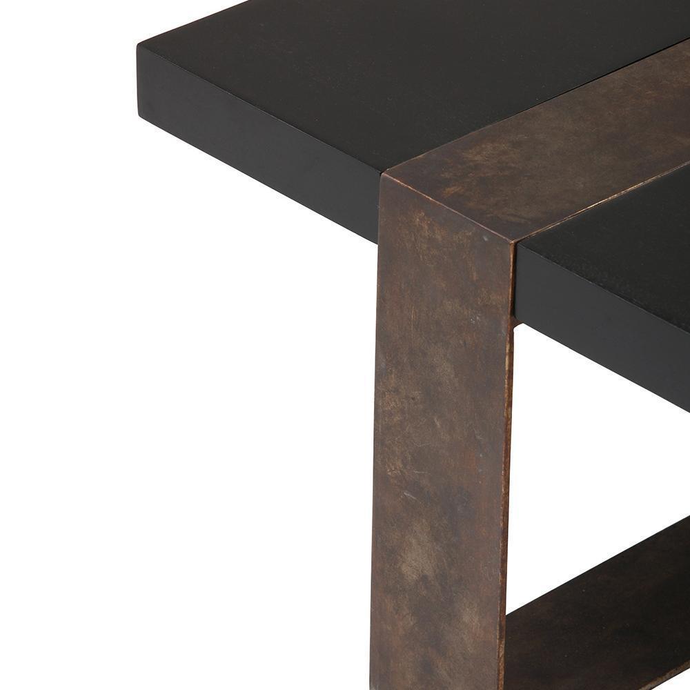 Close-up of a modern block table corner showing a matte black solid wood tabletop intersecting a wide mahogany-toned metal leg with an industrial, slightly weathered finish.