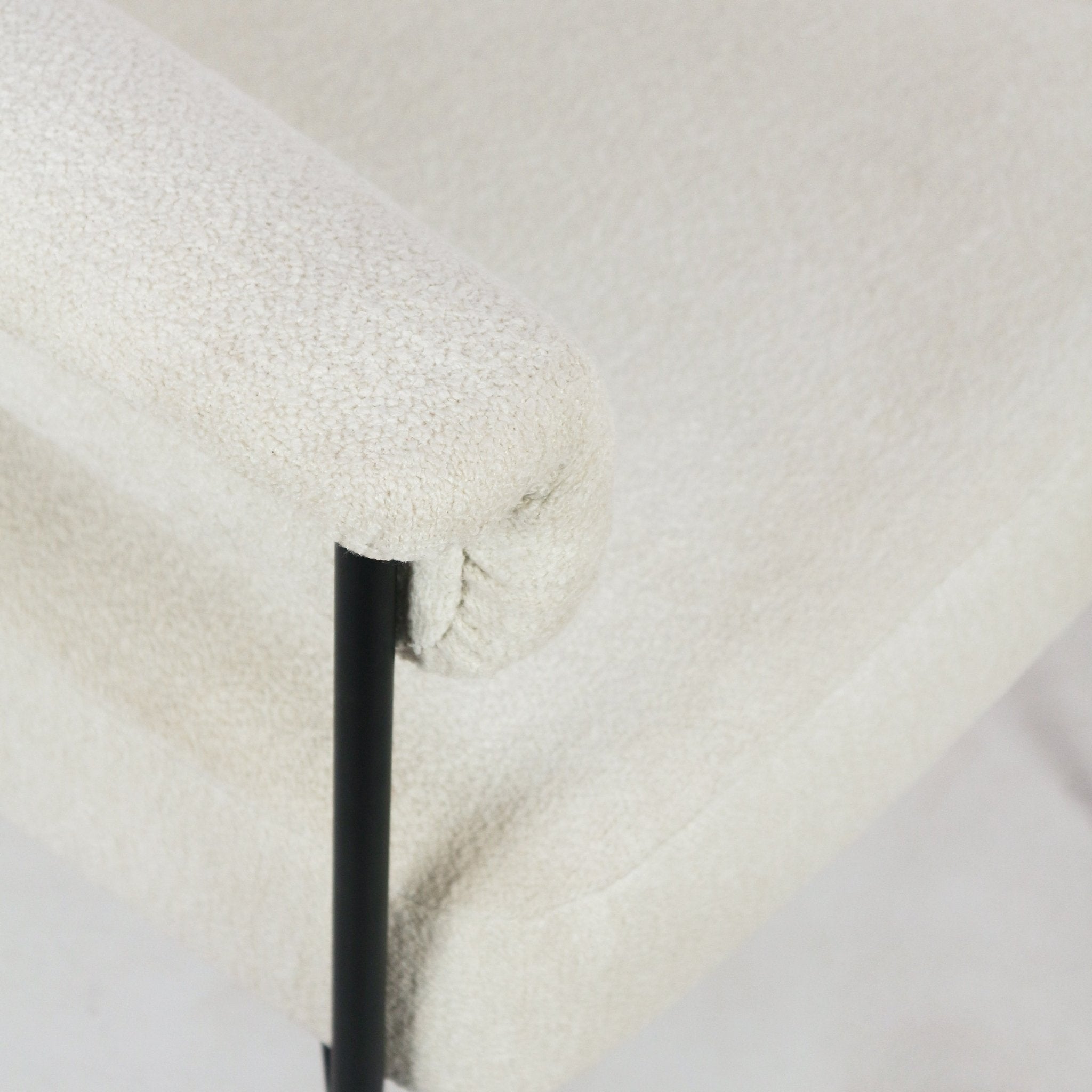 Close-up of a cream boucle upholstered dining chair armrest and seat corner showing textured fabric, seam detail and a slim matte black metal support post.