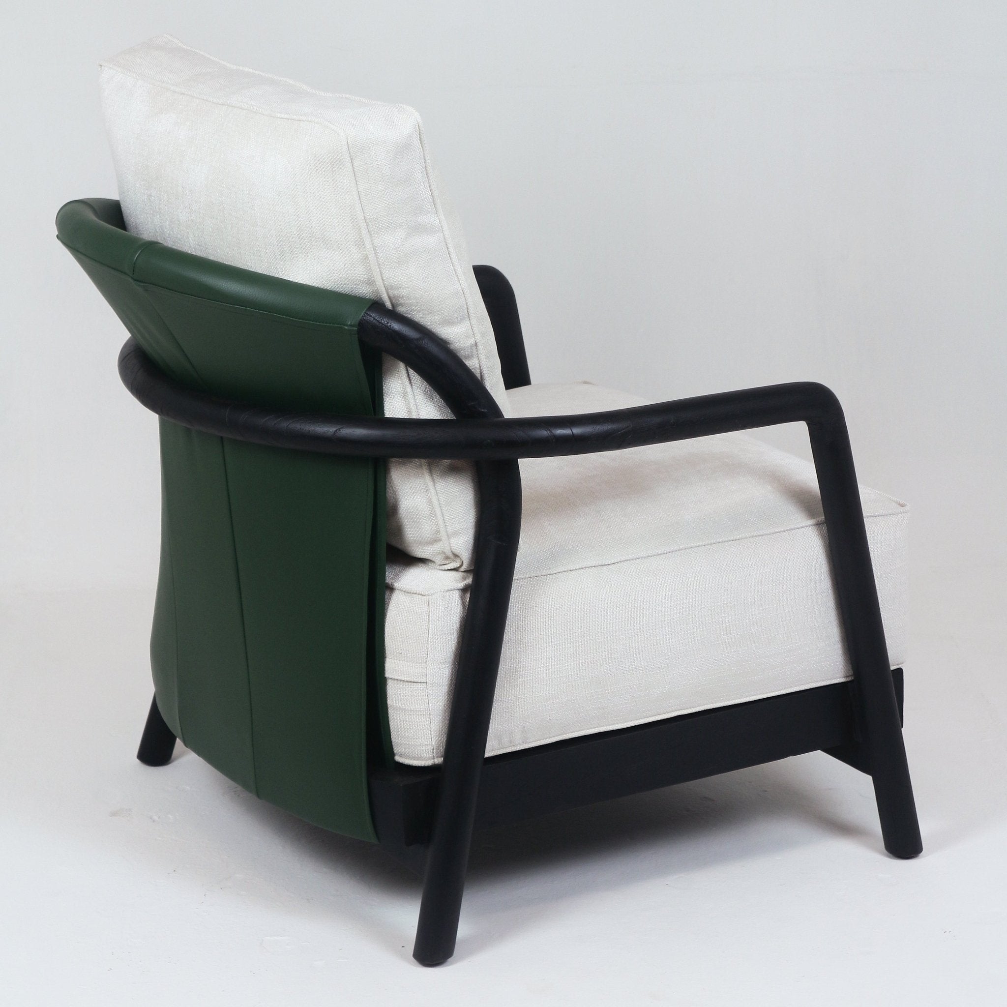 Side view of a mid-century modern armchair with a dark-stained solid teak frame and rounded arms, a deep green leather rear panel, and off-white fabric seat and back cushions.