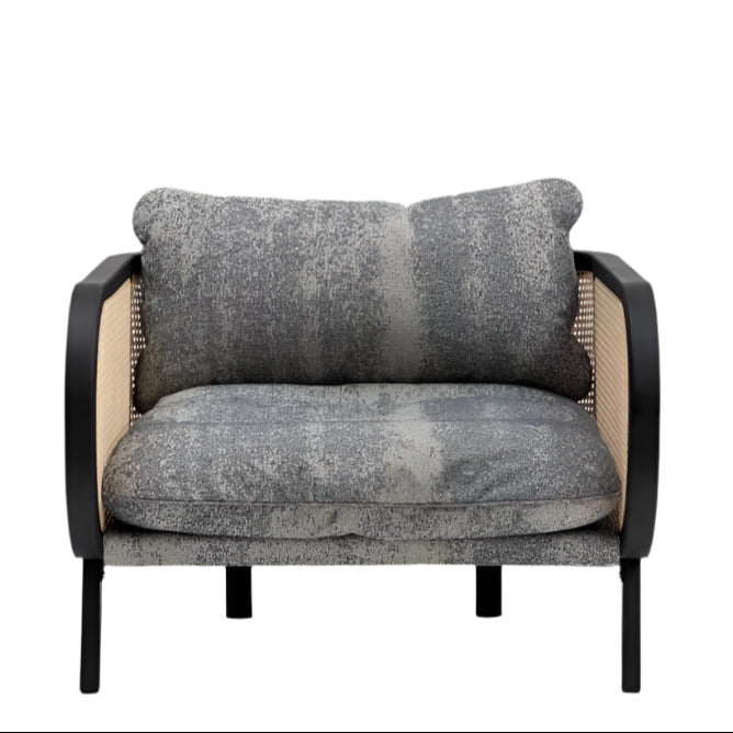 Front view of a modern cane lounge chair with a black wooden frame, natural woven cane side panels, and plush textured gray fabric seat and back cushions on slim black wooden legs.