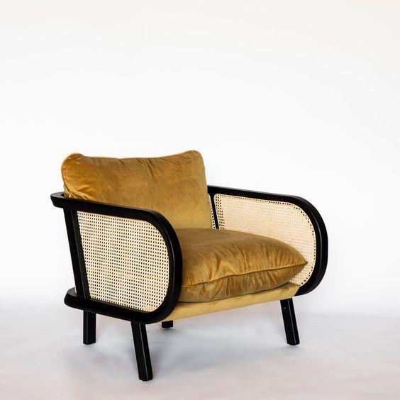 Low-profile lounge chair with a mustard velvet seat and loose back cushion, black curved wooden frame with woven cane side panels and short tapered legs, photographed on a plain white background.