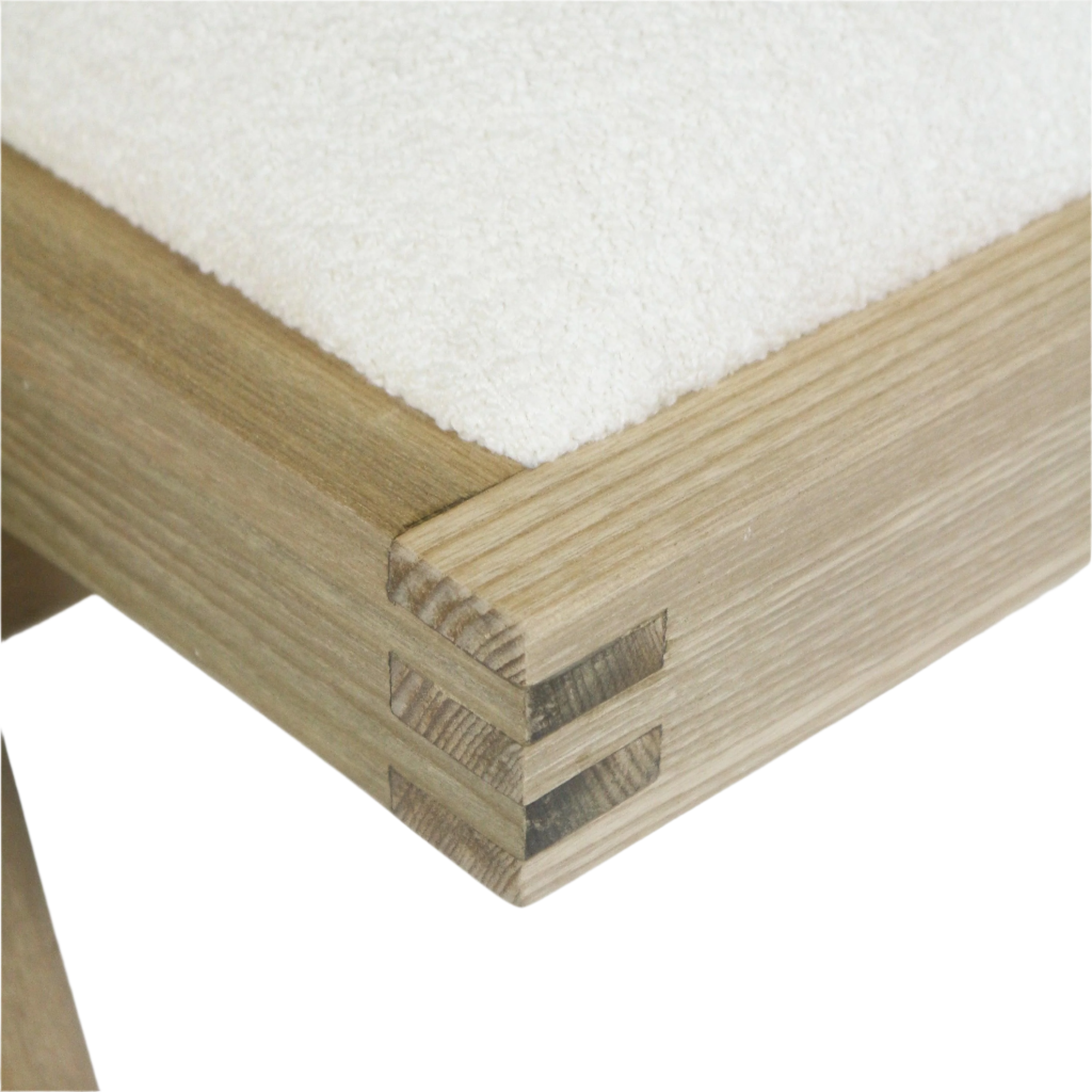 Close-up of a natural blonde wood dining chair corner showing a three-tier finger-joint detail and a cream-beige boucle upholstered seat cushion.