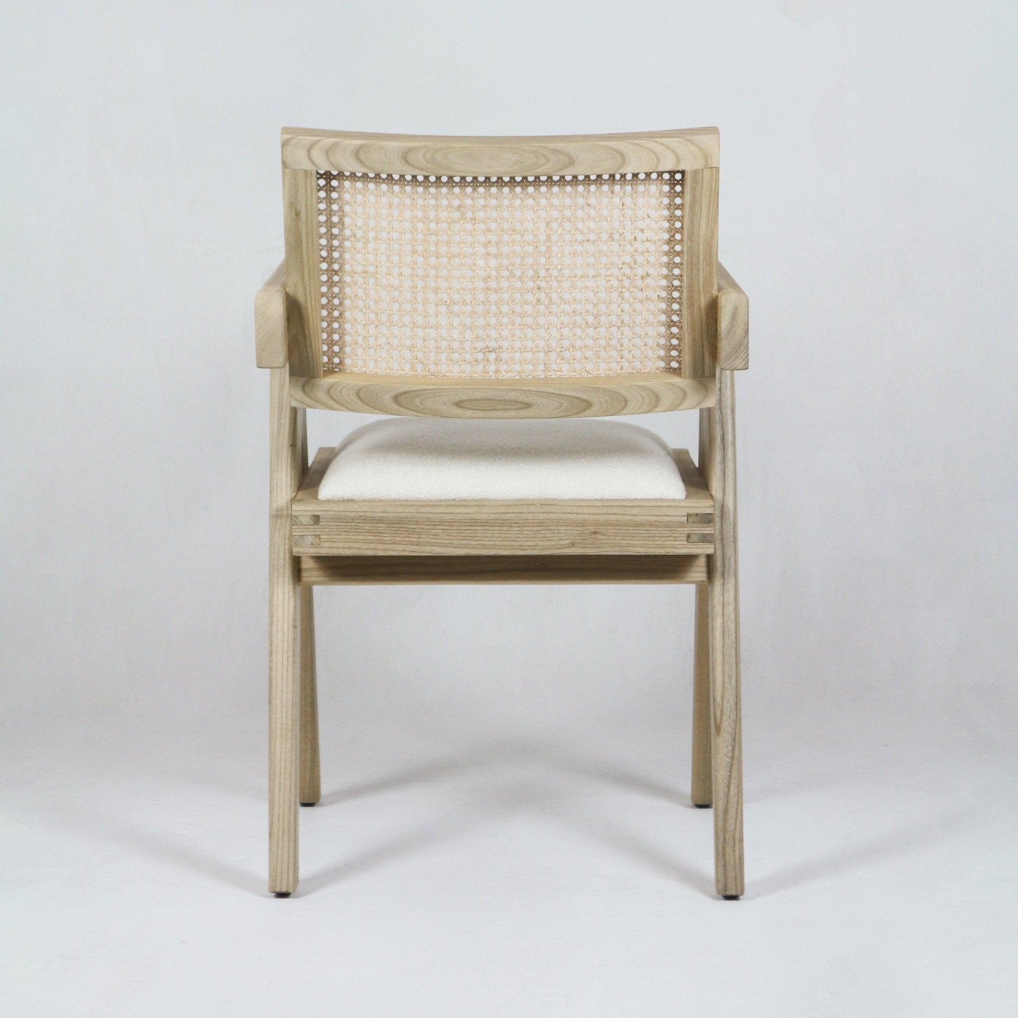Front view of a mid-century modern dining chair in natural blonde wood with a woven cane back, off-white upholstered seat cushion and slim armrests, photographed on a plain white background.