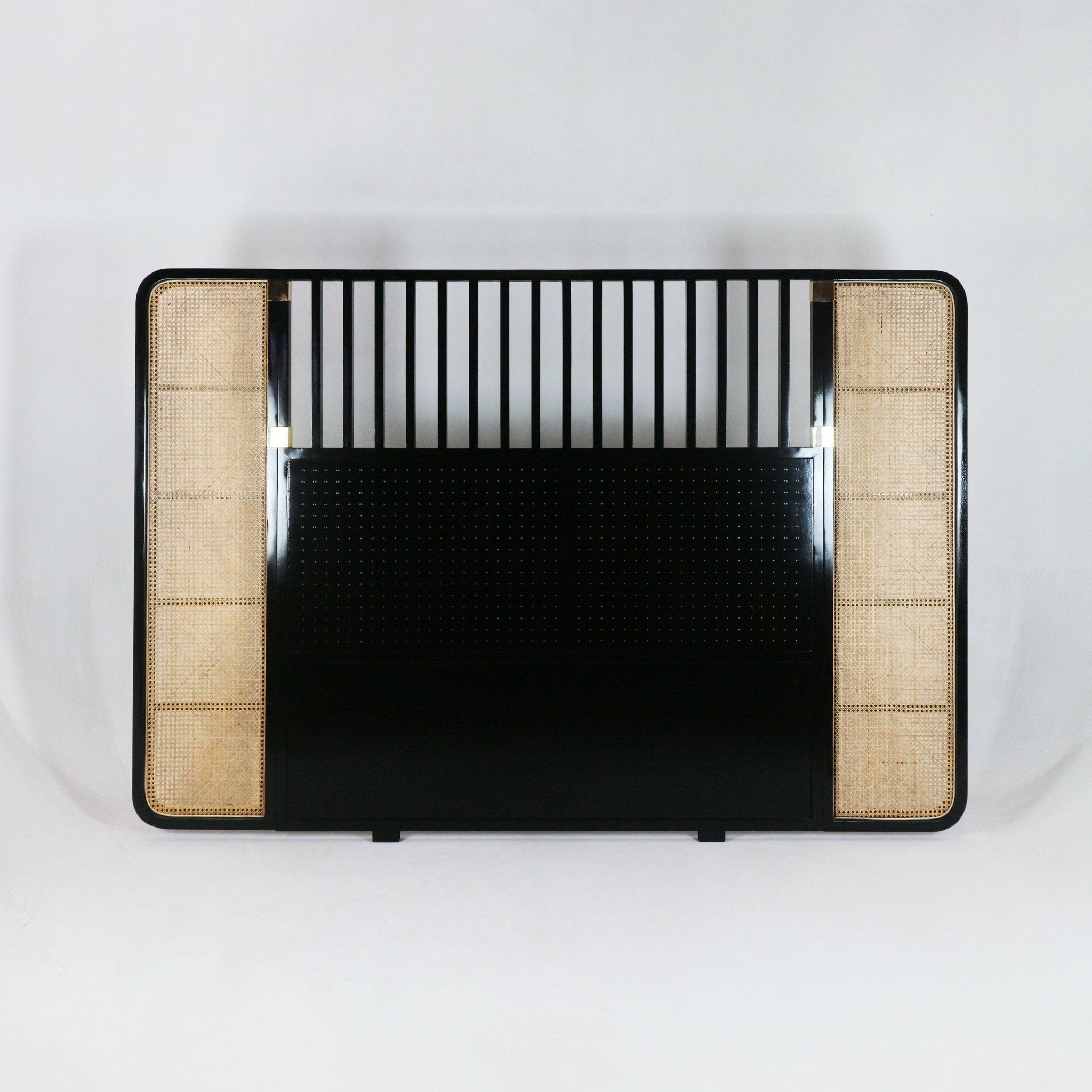 Boho-style king headboard in black metal and oak with natural rattan cane panels on both sides, vertical slat detailing across the top and a solid black central panel.