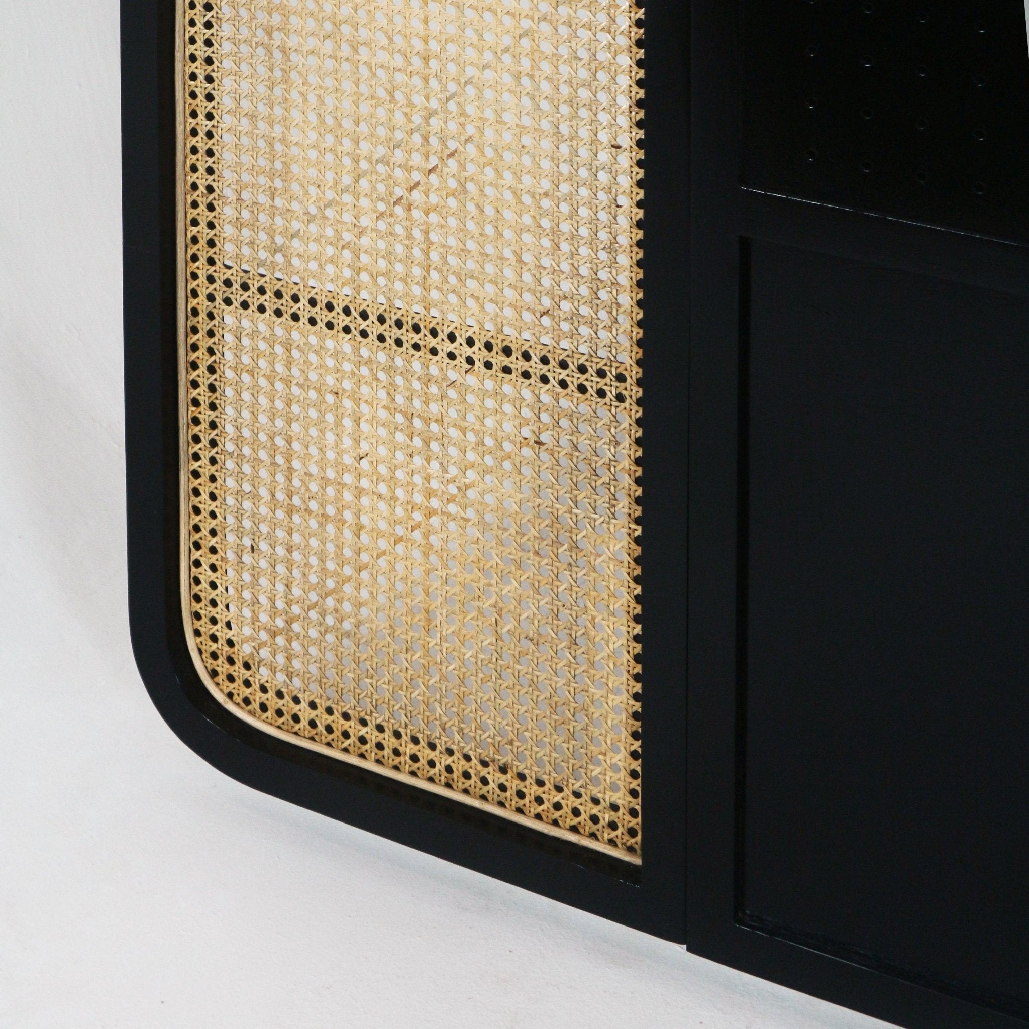 Close-up of a black oak headboard frame featuring a woven natural cane rattan panel with rounded corner and contrasting blond rattan detailing.