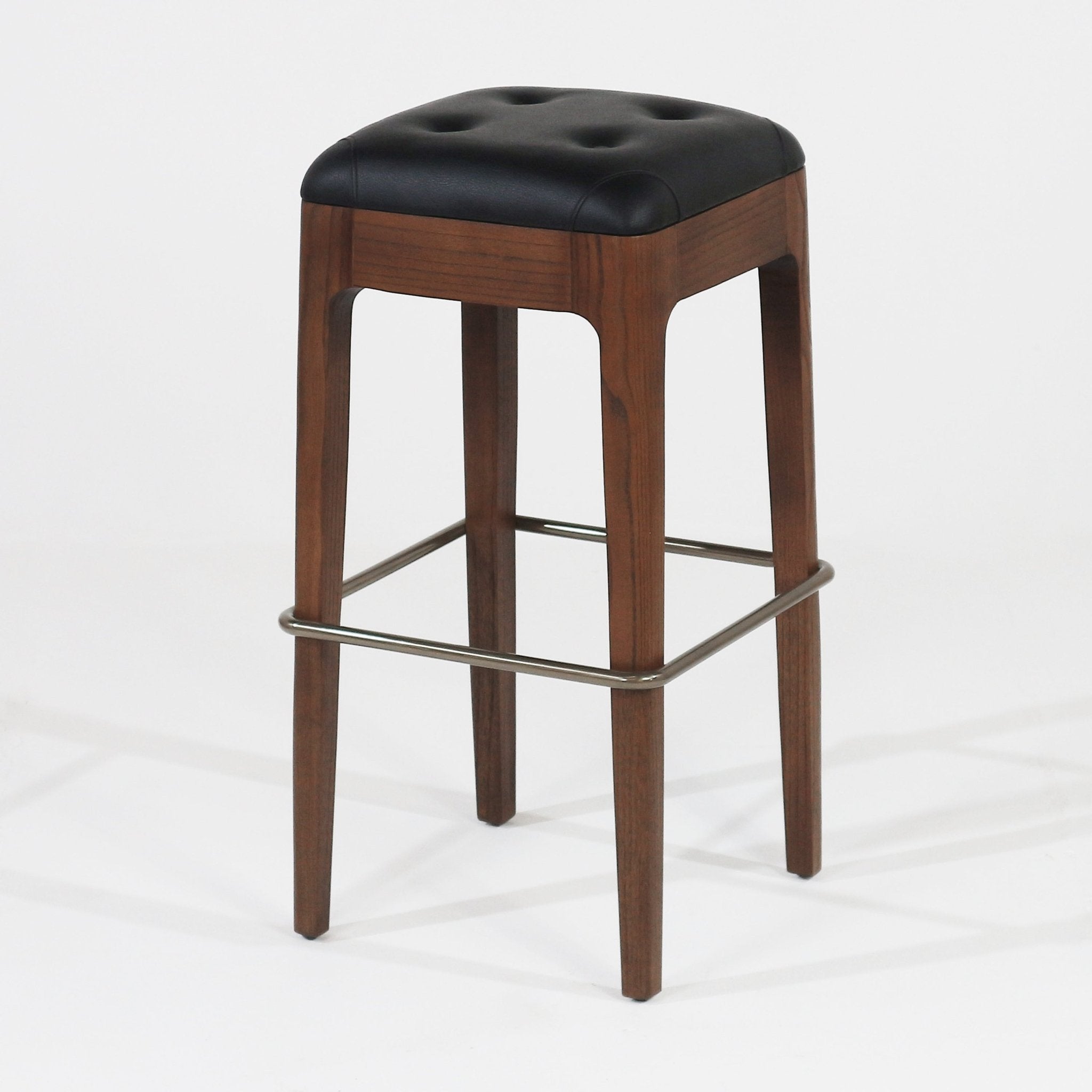 Backless counter stool with a black tufted leather seat atop a walnut wood frame, tapered legs and a square brushed-metal footrest.