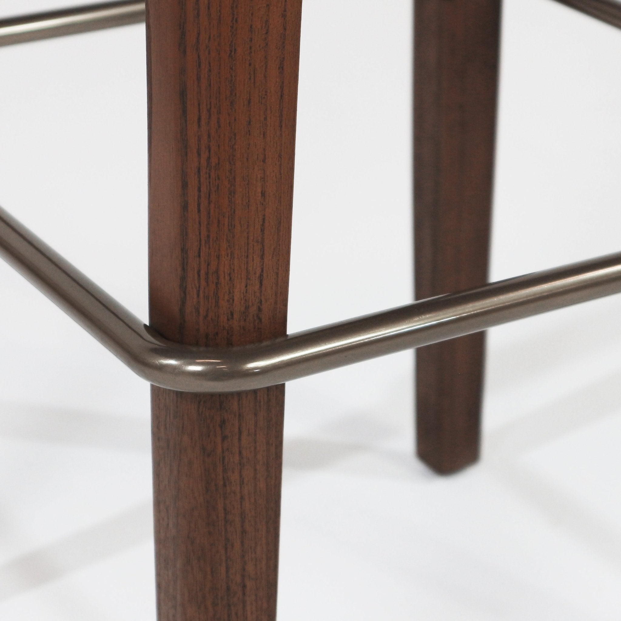 Close-up of walnut wood stool legs and a brushed black metal footrest rail, highlighting the walnut grain and rounded metal support.