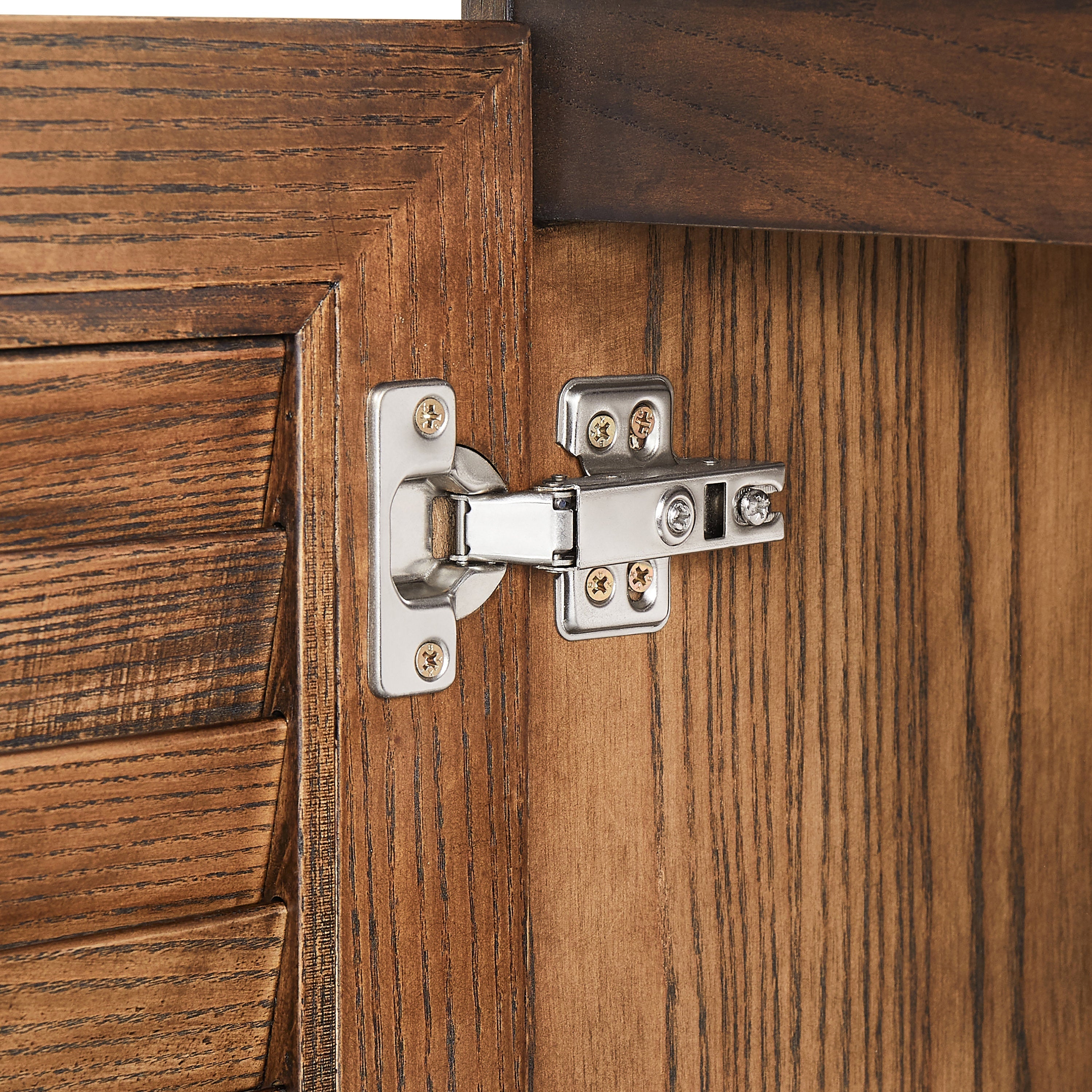 Close-up of a polished metal hinge mounted on a walnut-finish natural wood vanity door interior, showing the mounting plate, gold-tone screws and pronounced wood grain detail.