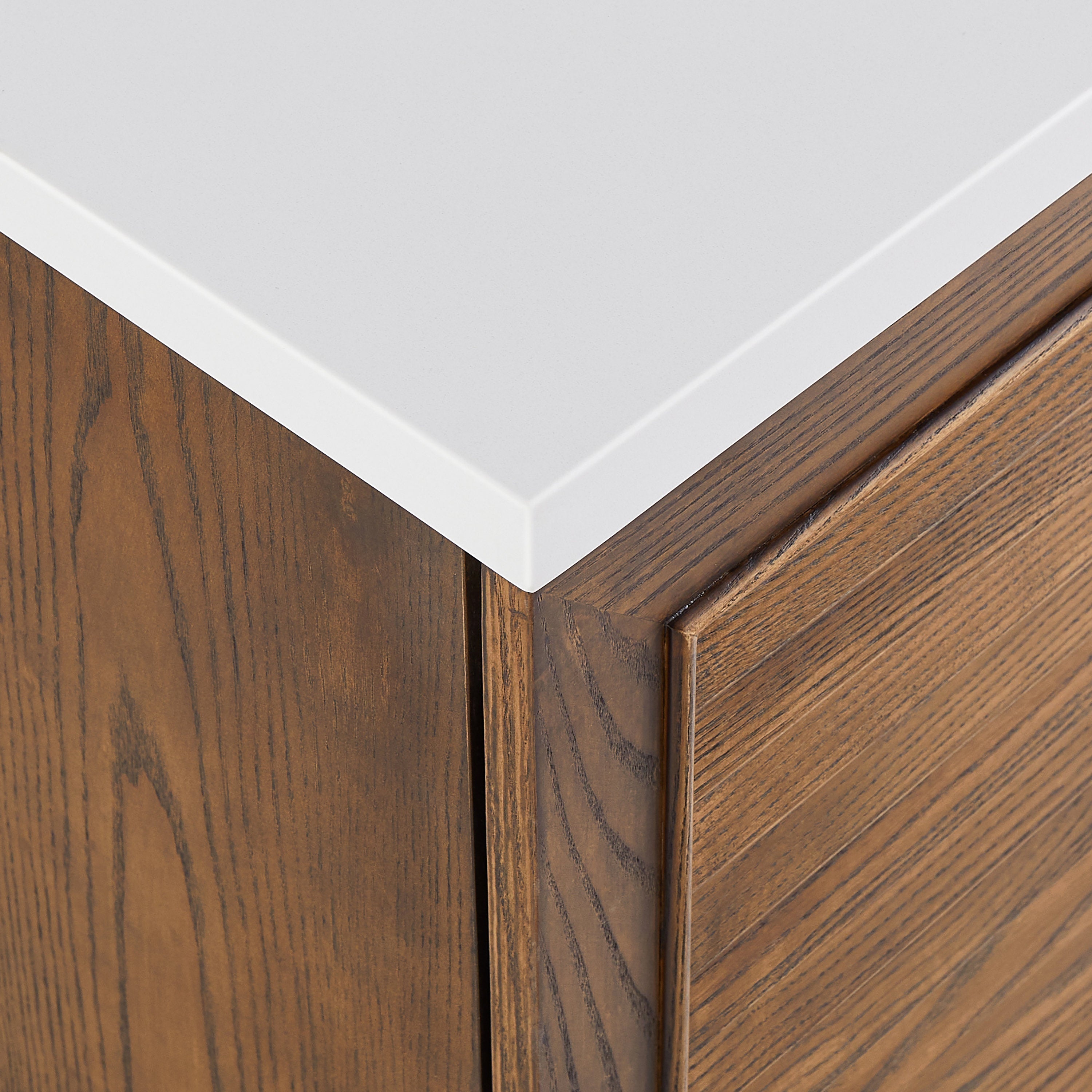 Close-up corner of a modern walnut bathroom vanity showing a pure white quartz countertop over a natural walnut wood cabinet with visible grain, mitered corner and beveled edge.
