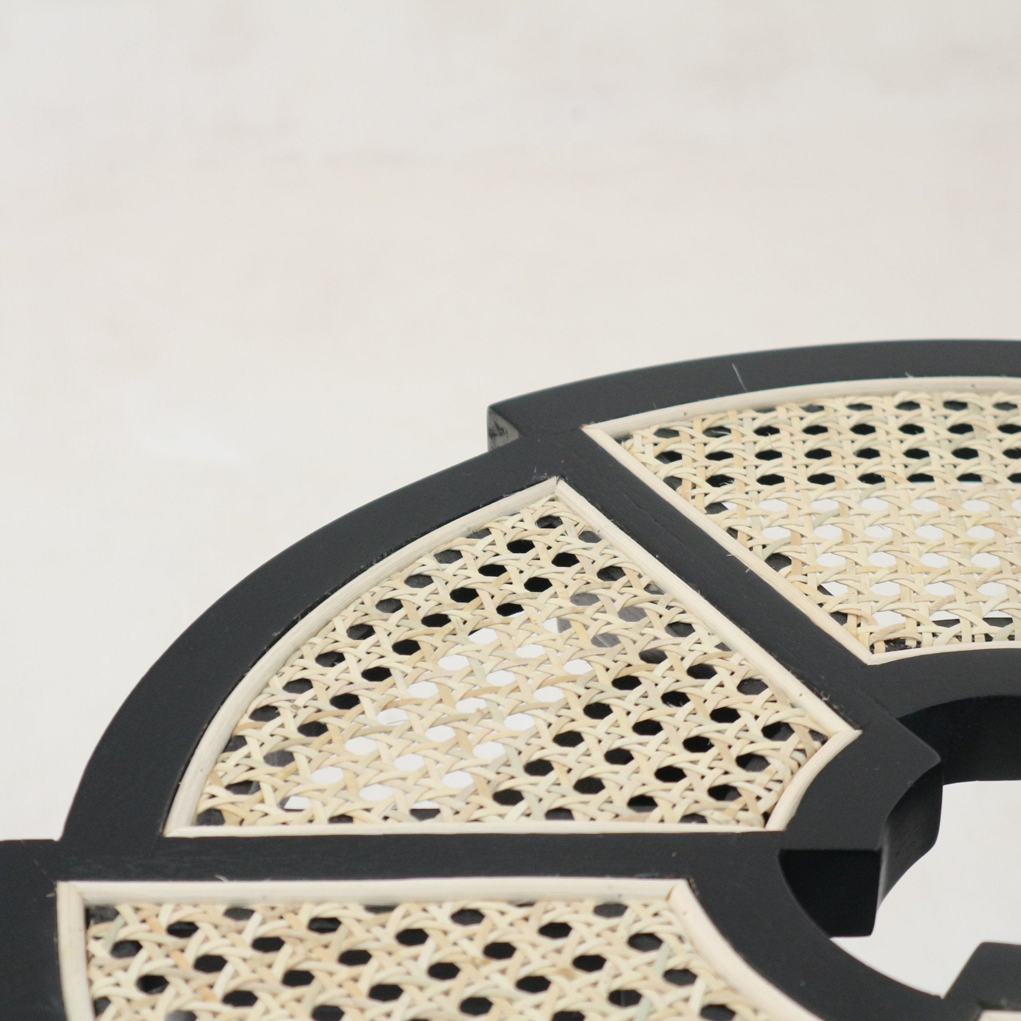 Close-up of a black-gloss wooden side table top featuring natural cream woven cane (rattan) panels set into segmented geometric frames, highlighting the cane weave and black wood trim.