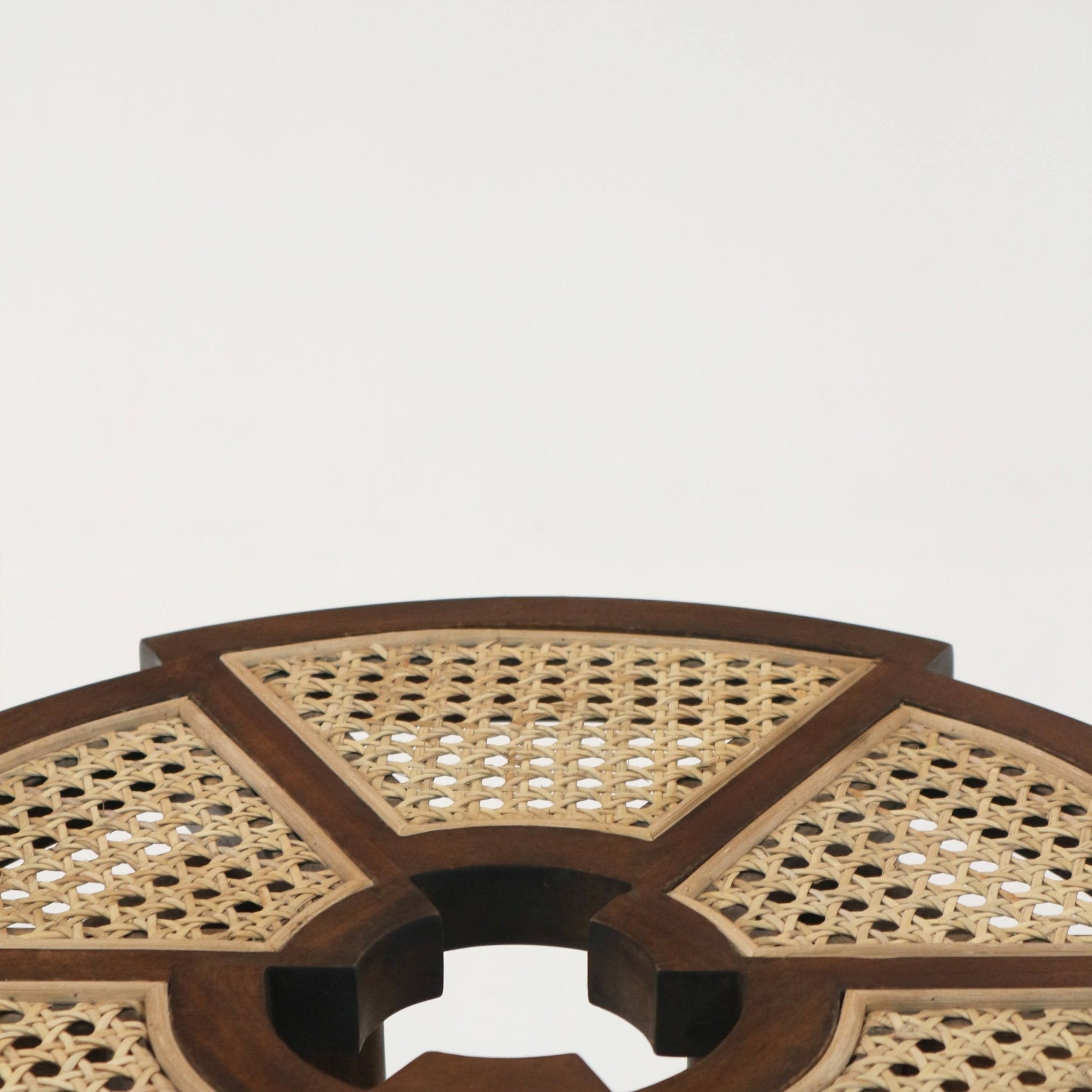 Close-up of a round teak-brown solid wood side table top with segmented panels of natural woven cane rattan and a central circular cutout, showcasing mid-century modern styling and warm wood grain.