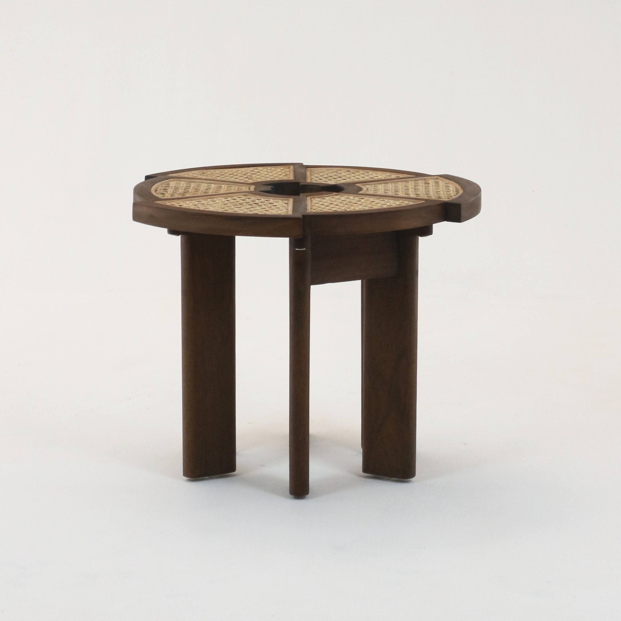 Medium brown teak side table with a round top featuring woven rattan cane in four pie-shaped panels and three solid wooden legs, photographed on a white studio background.