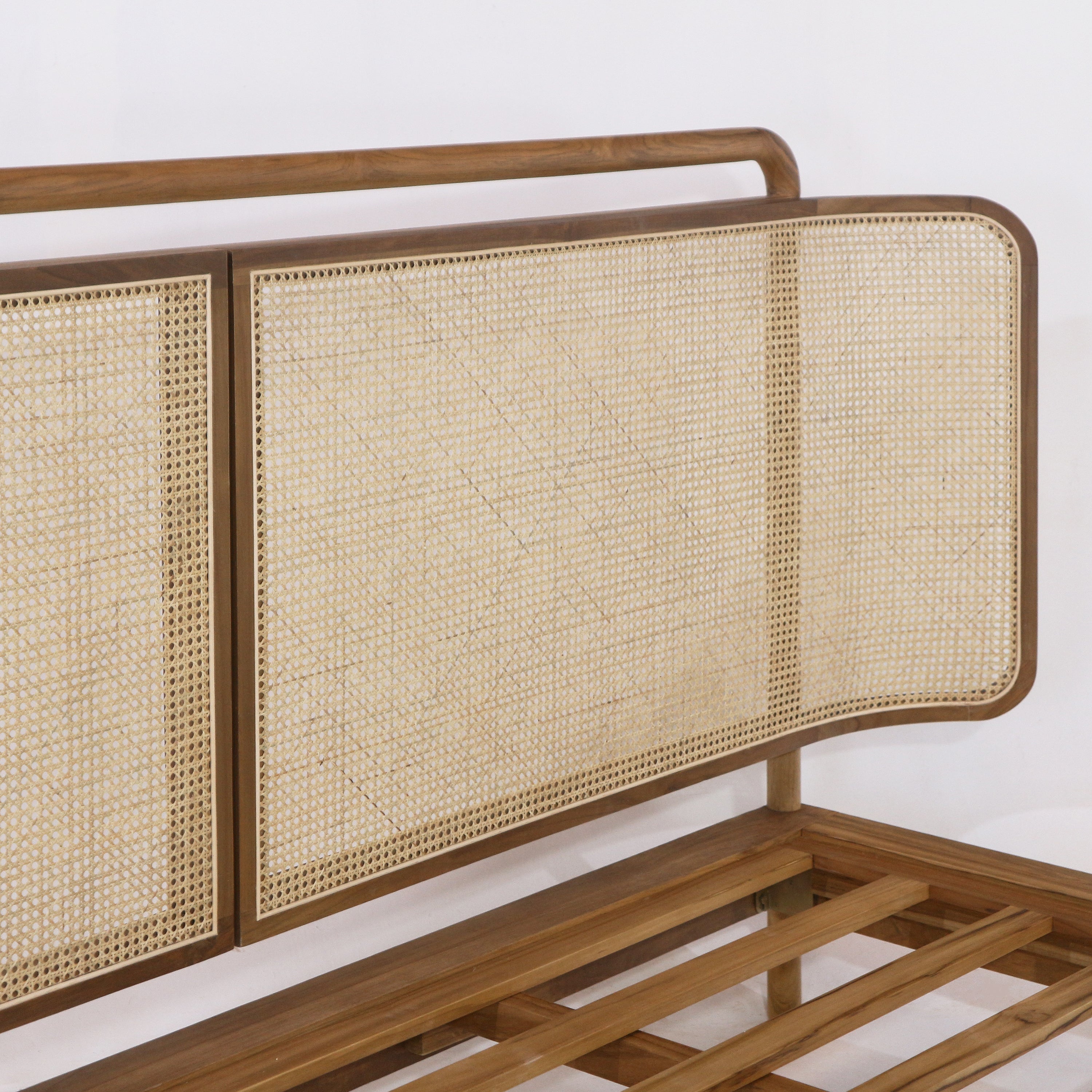 Close-up of a natural teak wood bed headboard with woven rattan cane panels and rounded frame edges, showing the teak platform slats beneath.