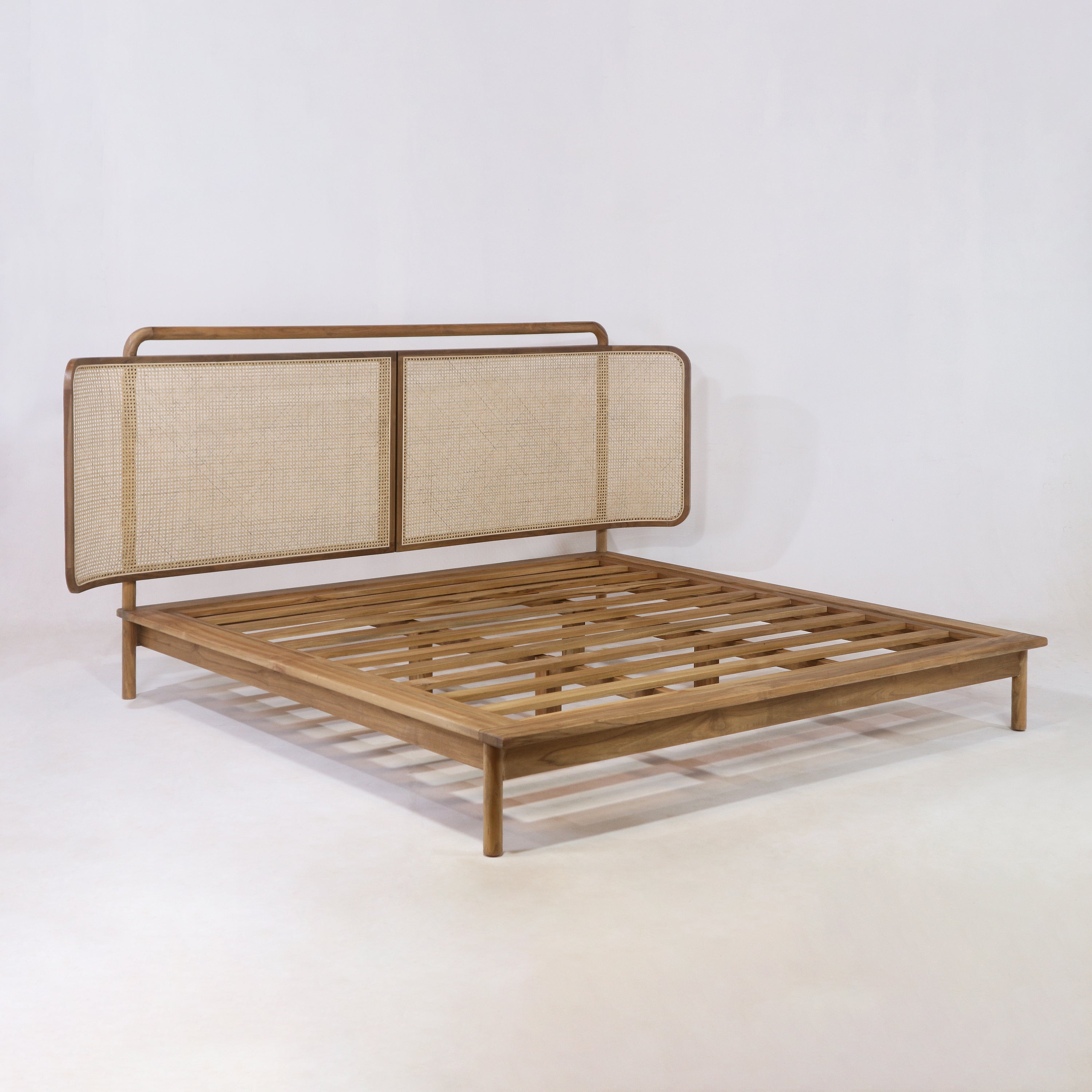 Boho-style low-profile teak platform bed with slatted wooden base and a woven rattan headboard in a natural teak finish, photographed on a white studio background.