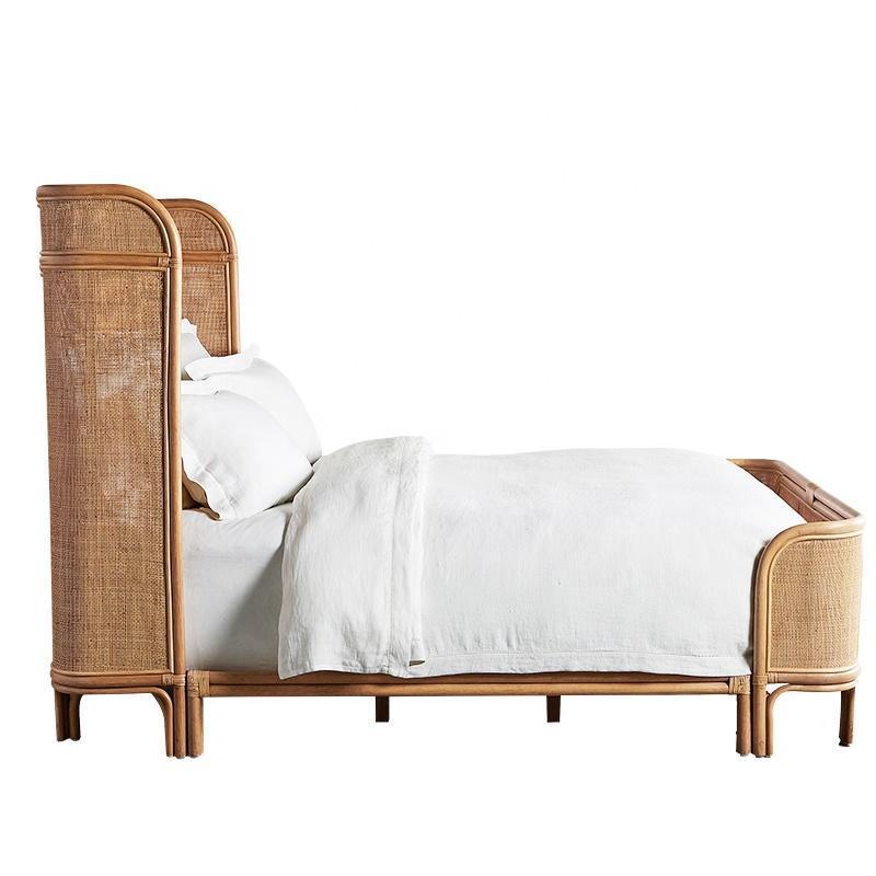 Side view of a teak and woven rattan platform bed with a tall curved headboard and rounded footboard in natural teak finish, styled with crisp white linens.