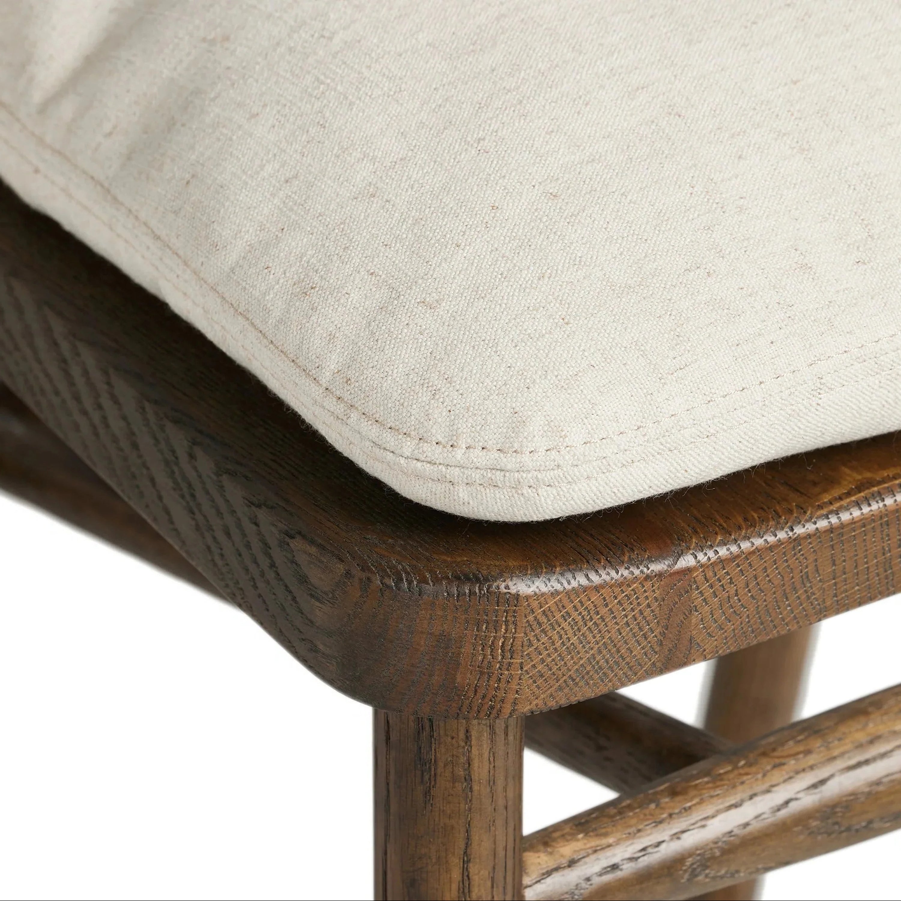 Close-up of a cream fabric cushioned seat on a natural wood counter stool frame, showing the stitched cushion edge, rounded wood seat corner and visible rustic wood grain.