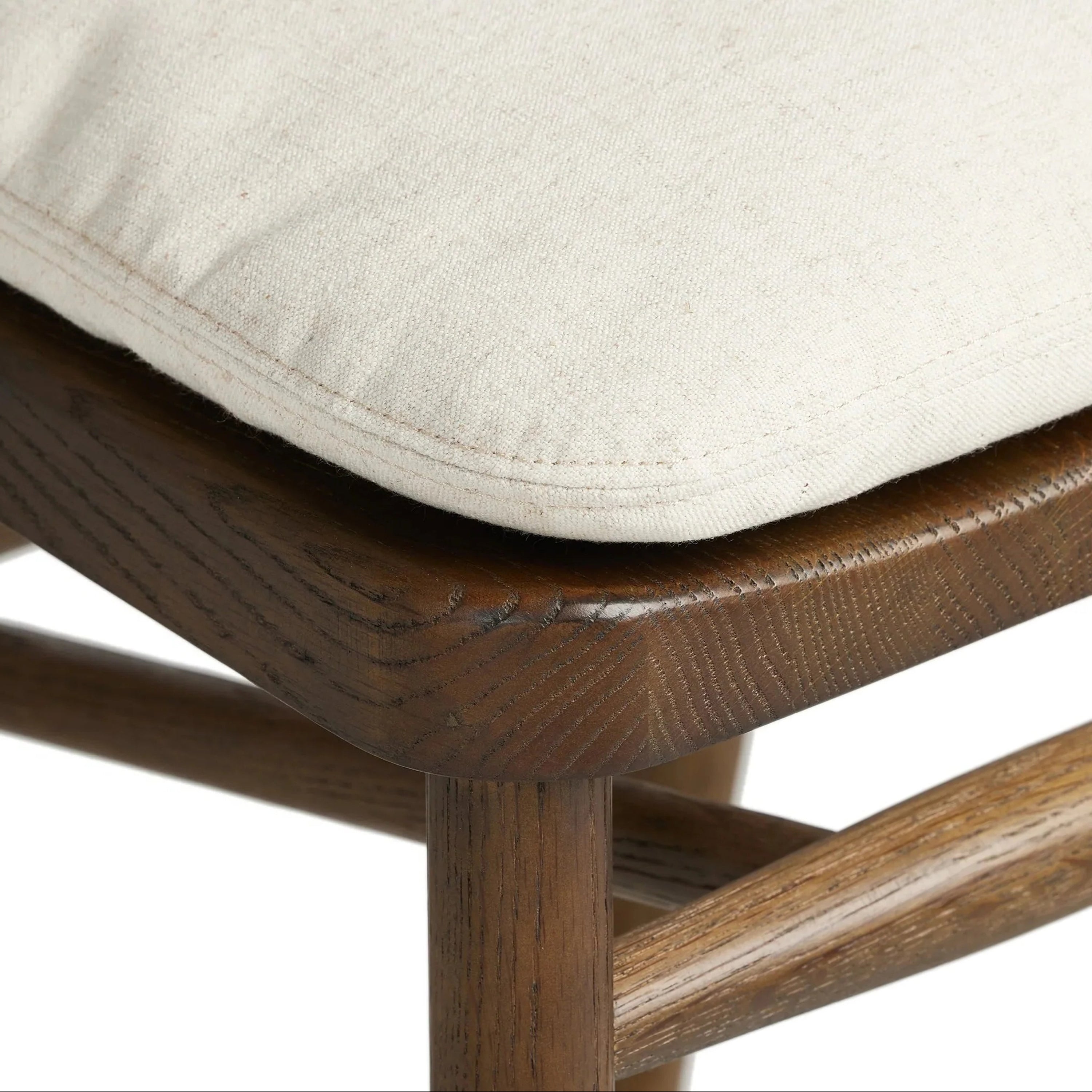 Close-up of a natural beige fabric cushion with visible stitched edge resting on the rounded top of a natural wood counter stool, highlighting the wood grain, joinery and textured upholstery.