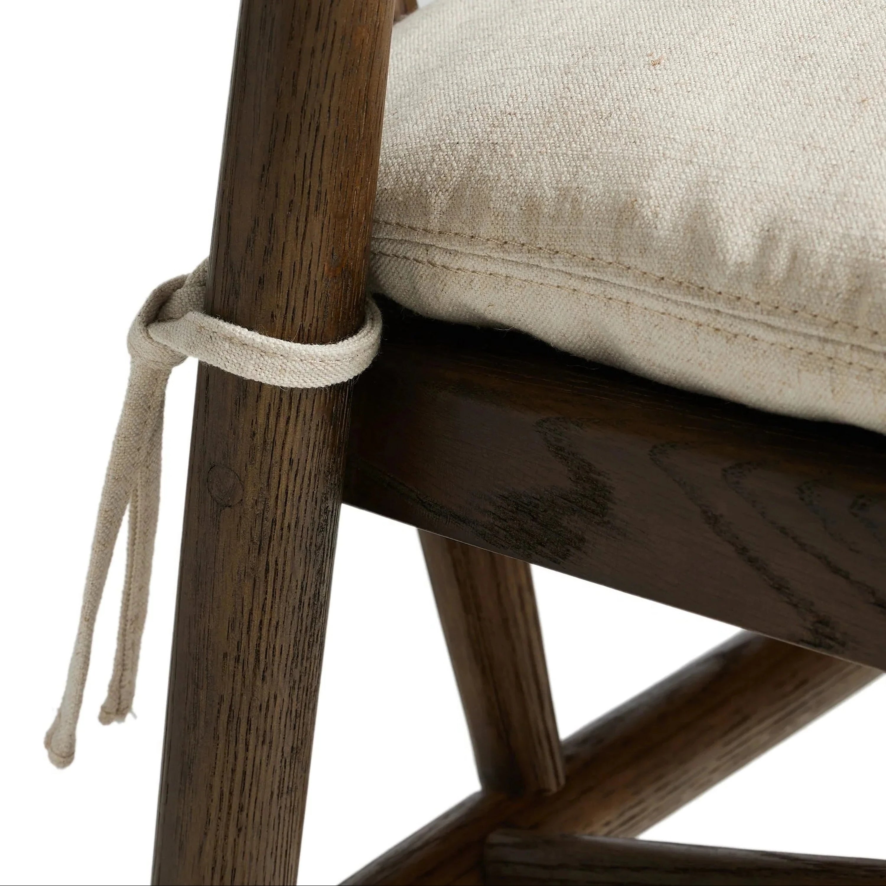 Close-up of a natural wood stool frame with a beige fabric cushioned seat secured by a rope tie, showing wood grain, stitch detail, and joinery.