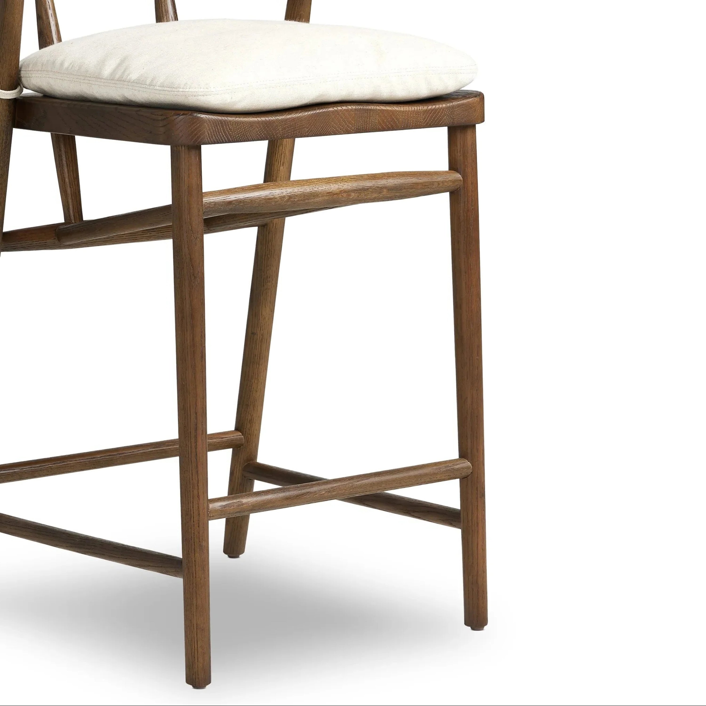 Close-up of a natural wood counter stool showing an off-white cushioned seat, tapered legs and crossed footrest stretchers in a warm natural finish, highlighting the wood grain.