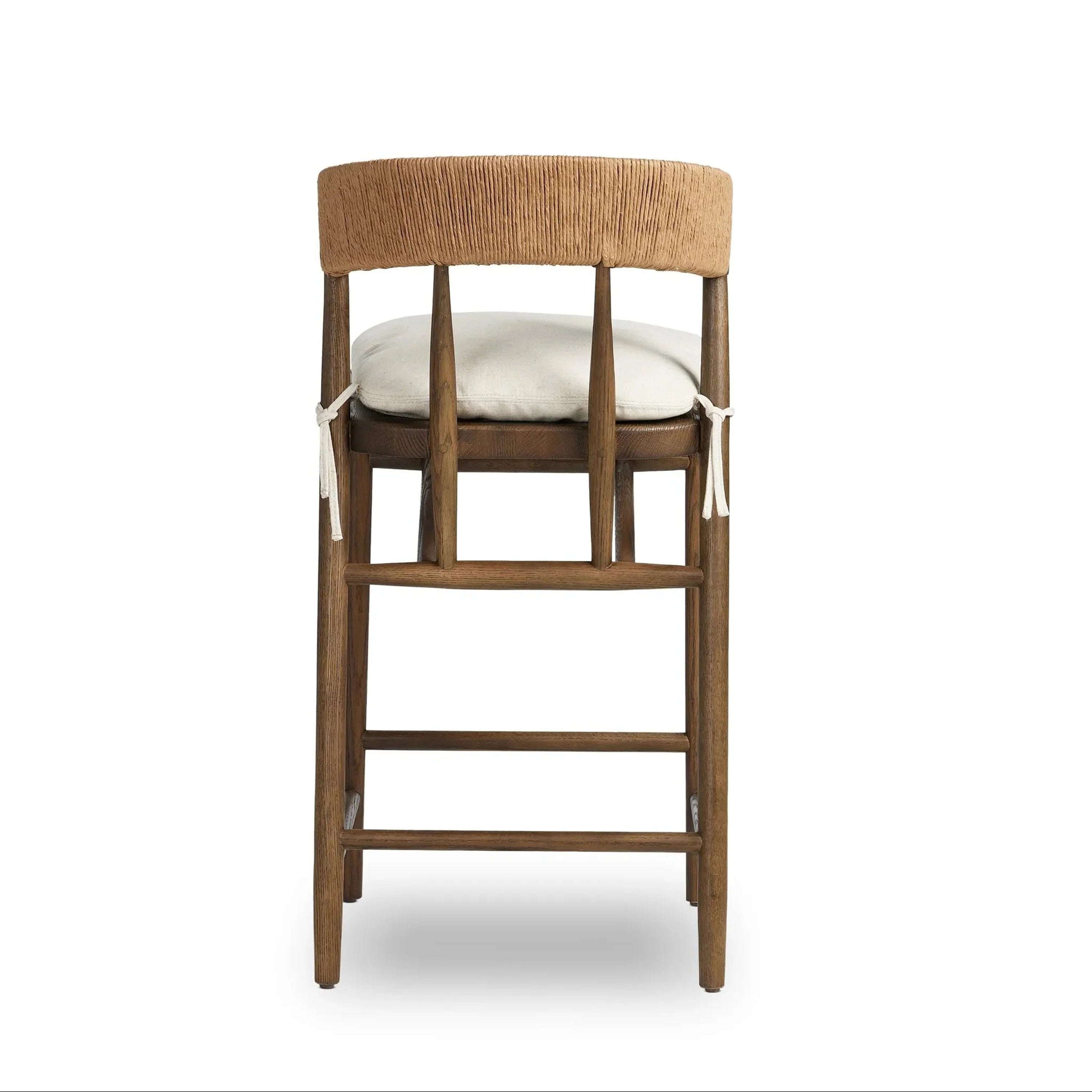 Rear view of a natural wood counter stool with a rope-wrapped C-shaped back, light beige fabric cushioned seat tied at the sides, and tapered wood legs with two horizontal footrest bars.