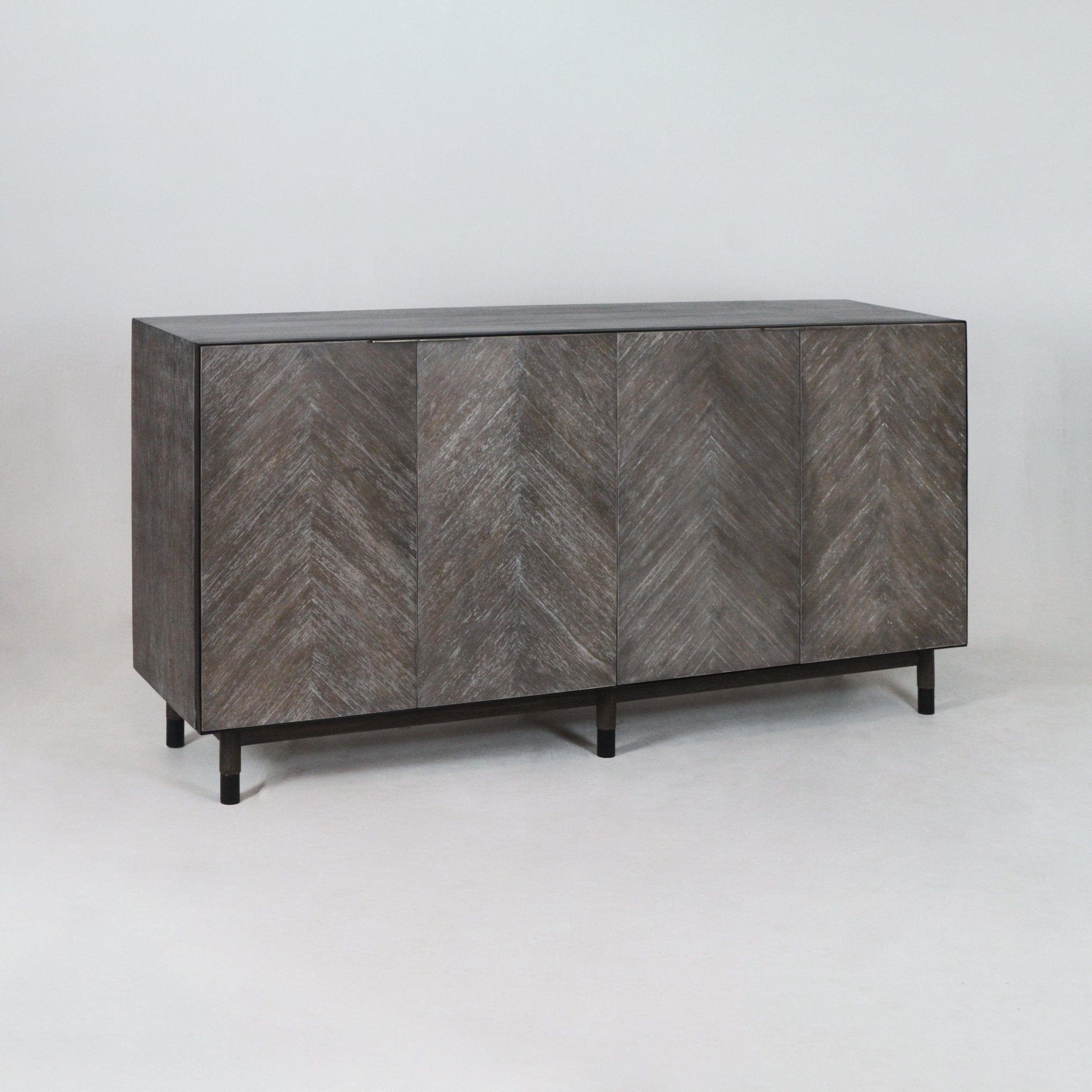 Mid-century modern teak sideboard with four herringbone-patterned doors in a weathered gray-teak finish, raised on slender black metal legs against a neutral background.