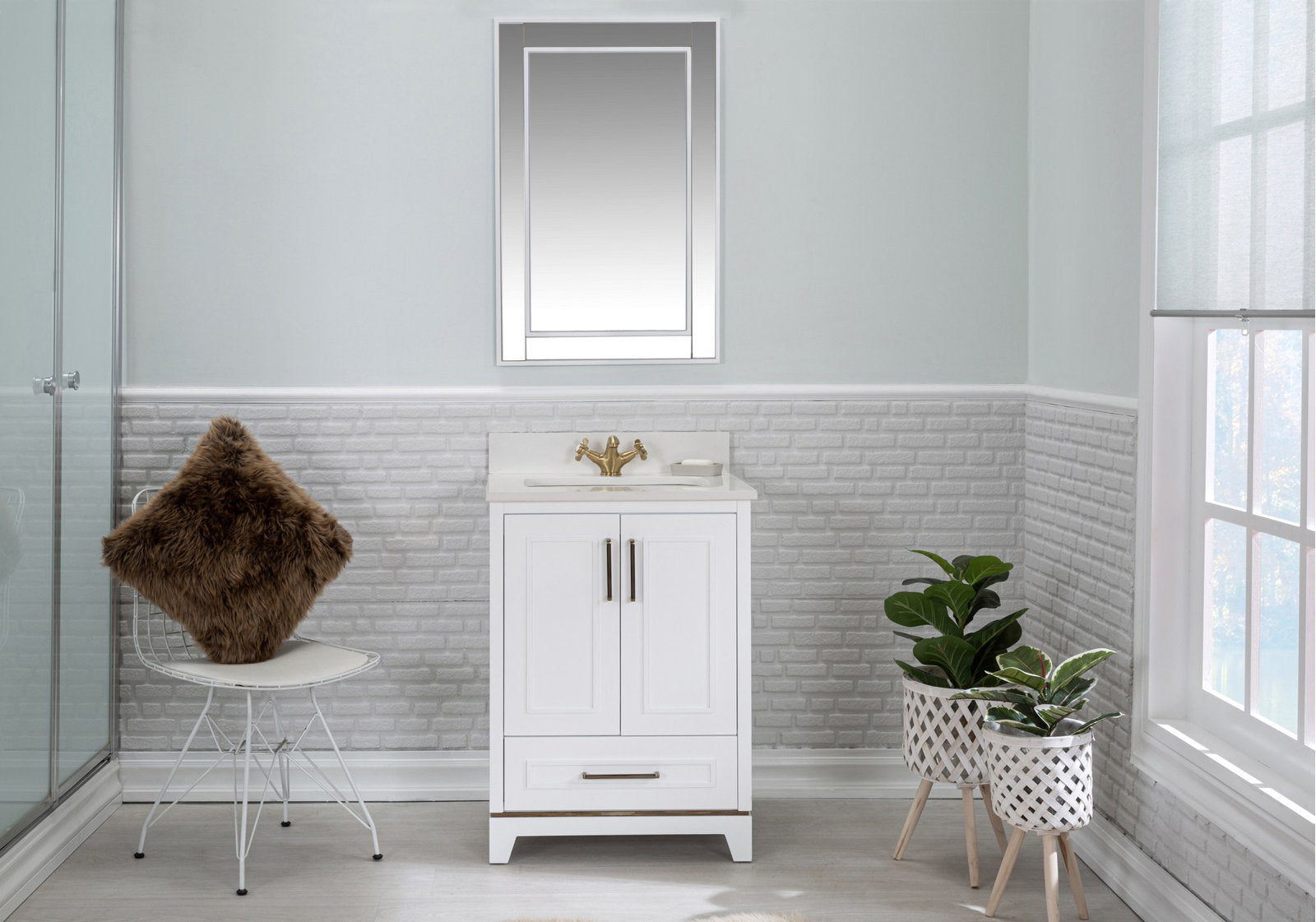 White modern solid wood single-sink vanity with a stone countertop and brass faucet beneath a rectangular mirror, staged in a pale gray half-brick bathroom with a wire chair and fur cushion and two potted plants by the window.