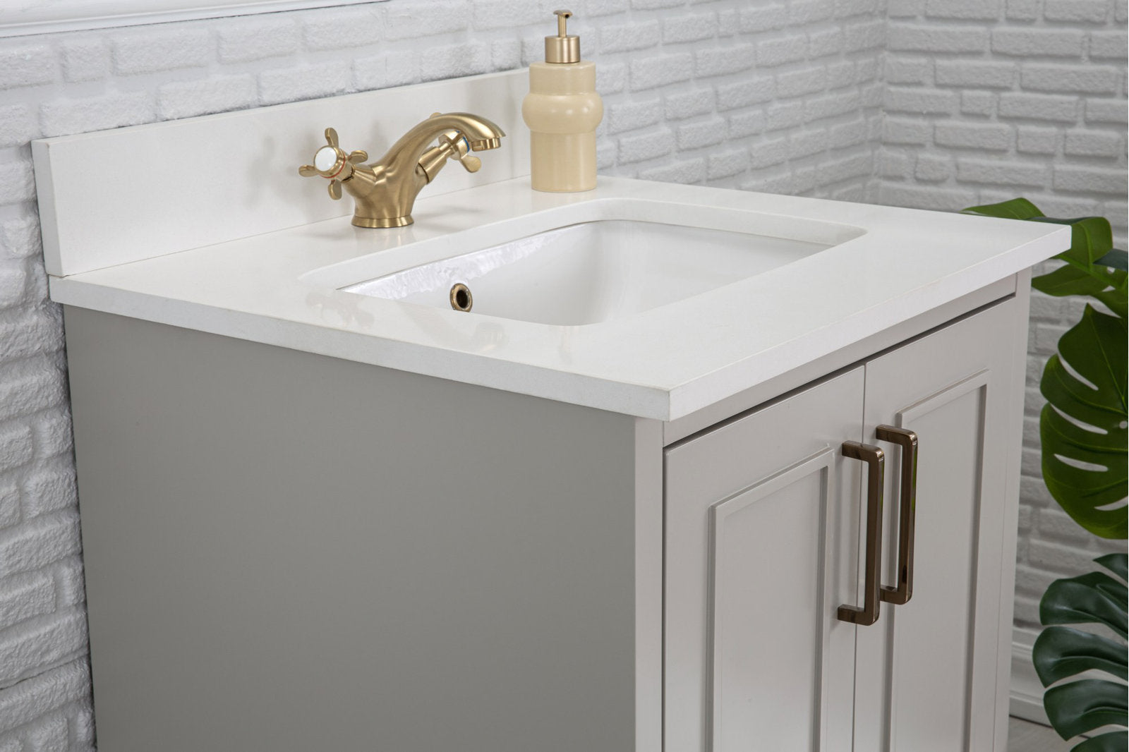 Modern solid wood bathroom vanity in stone finish with white stone countertop and integrated ceramic sink, brushed brass two-handle faucet, beige soap dispenser, and rectangular cabinet doors with bronze bar handles.