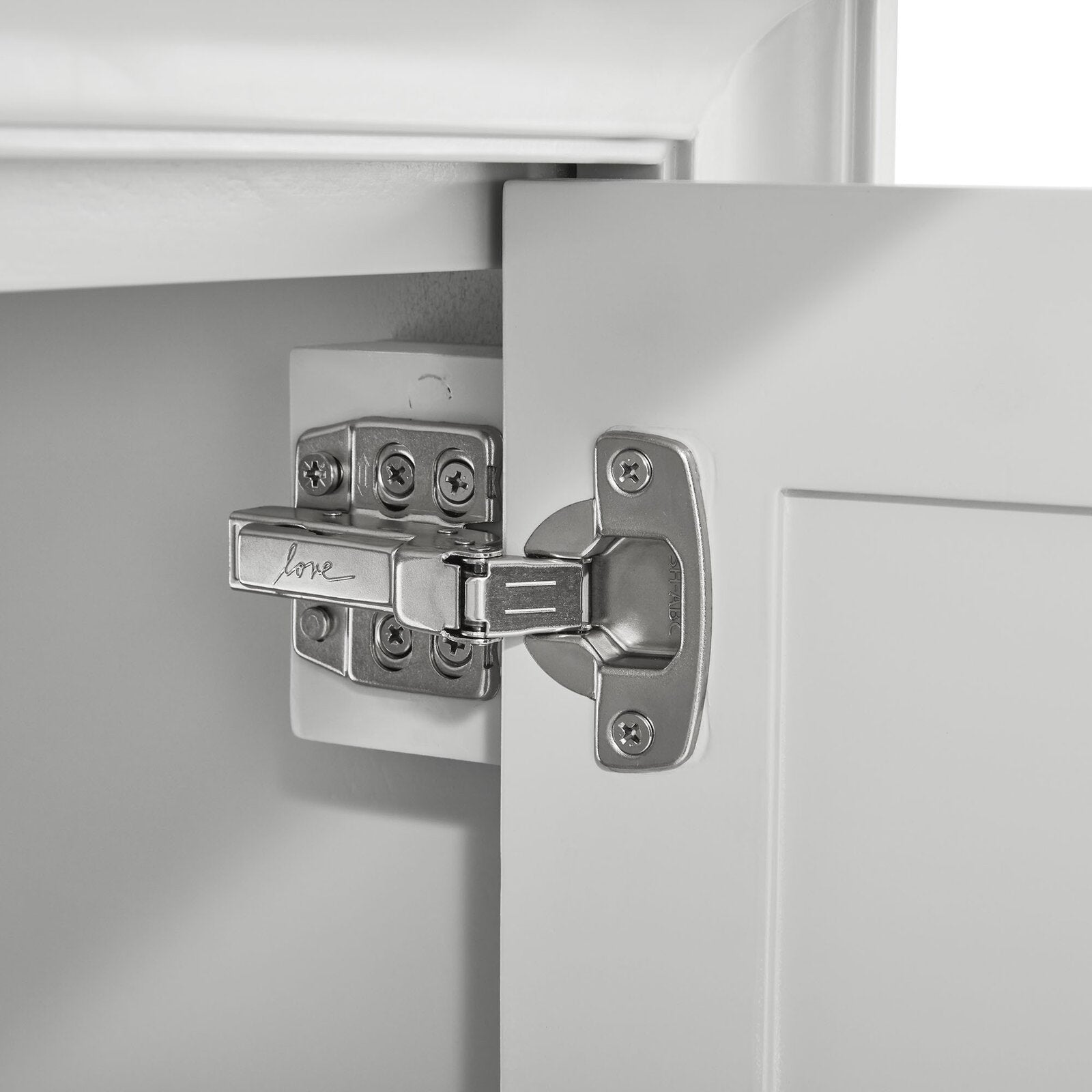 Close-up of a chrome soft-close cabinet hinge mounted to a white wooden bathroom vanity door and inner frame, showing screws, hinge cup and hardware details.