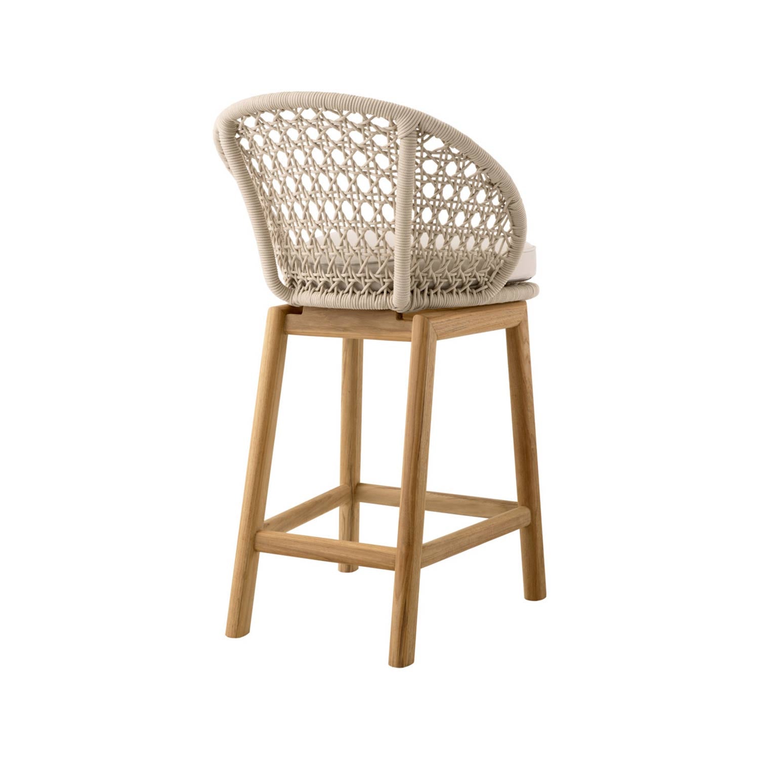 Rear three-quarter view of an armless outdoor bar stool with a natural teak frame, light beige rope-woven back, cream upholstered seat cushion and square teak footrest.