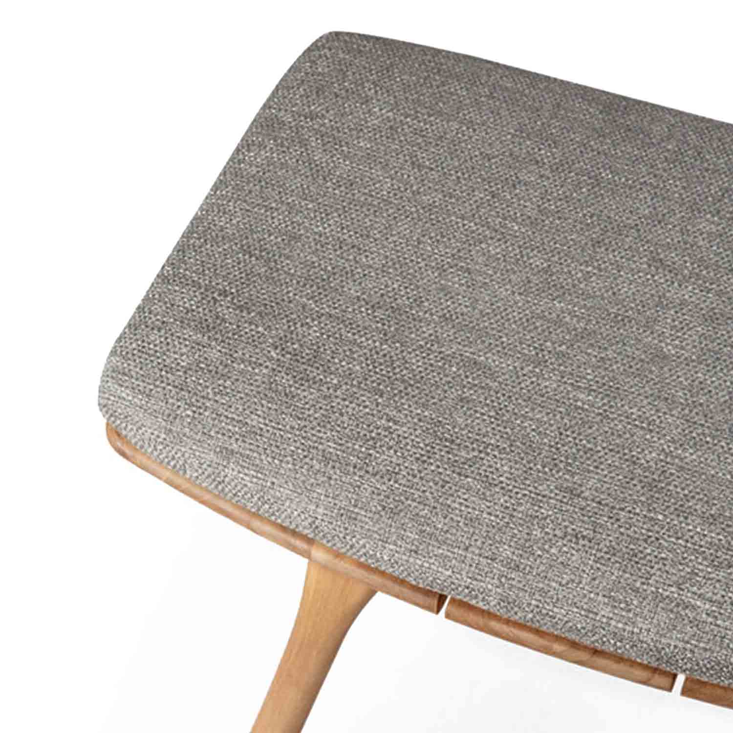 Close-up of an upholstered backless shower stool seat showing grey-beige textured fabric over a rounded teak edge and a tapered teak leg, coastal-style solid wood seating.