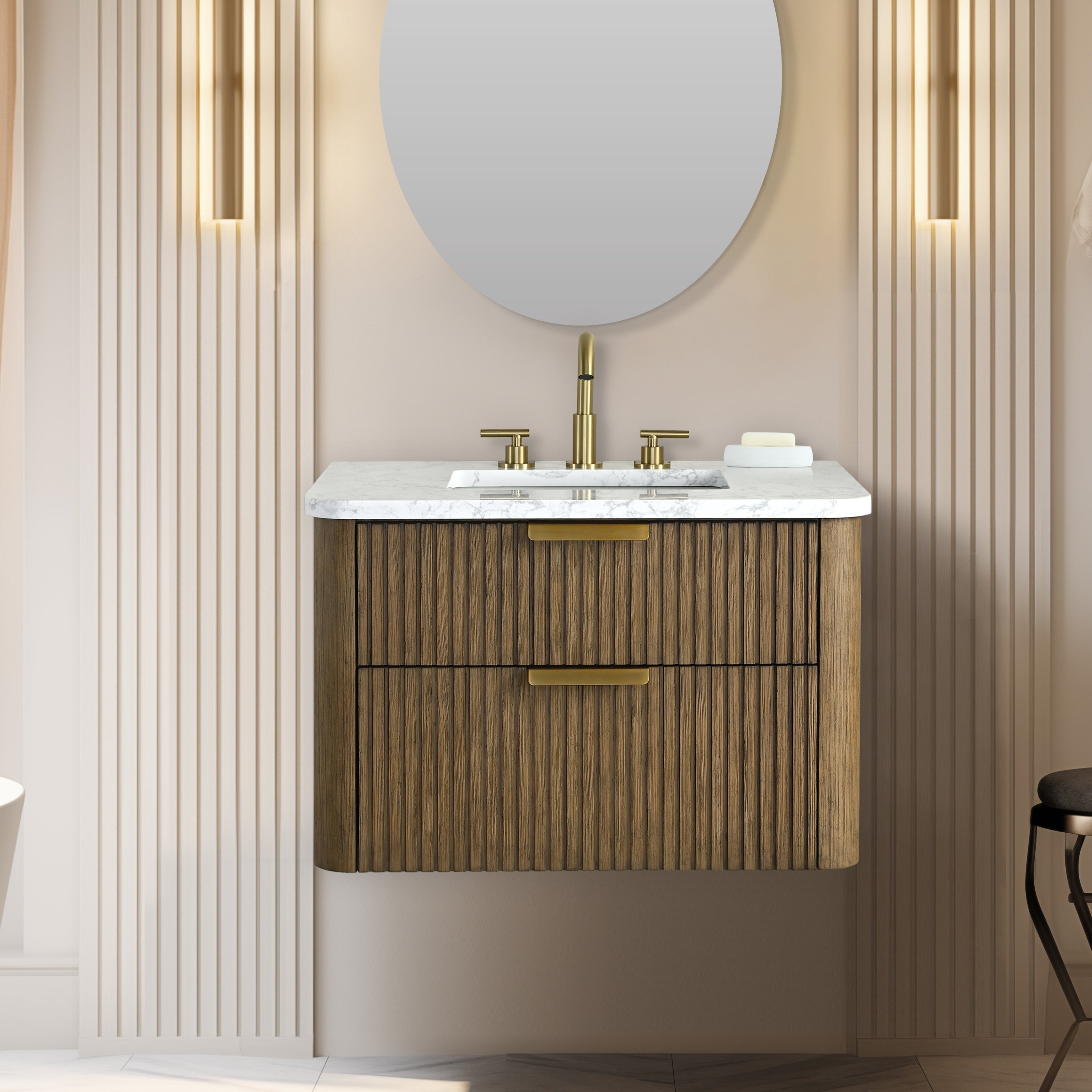 Floating fluted solid-wood vanity with white stone top, integrated rectangular sink, brass widespread faucet and matching drawer pulls, shown beneath a round mirror against beige vertical fluted wall panels.